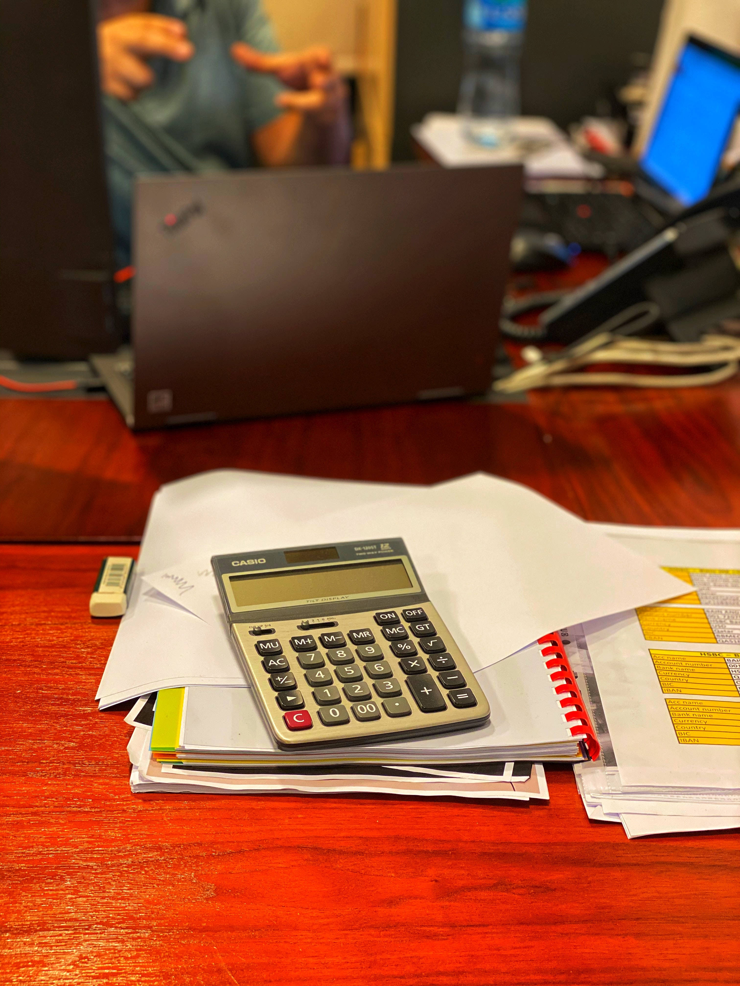Chartered Accountant 桌布 壁紙 — 一台 Casio 計算機放在一個雜亂辦公室中拋光木桌上的一疊文件和紅色線圈筆記本上。