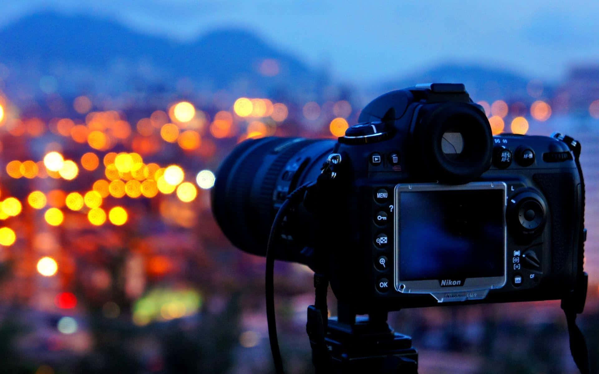 Dslr 桌布 壁紙 — 一台DSLR相機安裝在三腳架上，捕捉暮色中散景燈光點綴的城市景觀，溫暖的橙色燈光映襯著清冷的藍色天空。