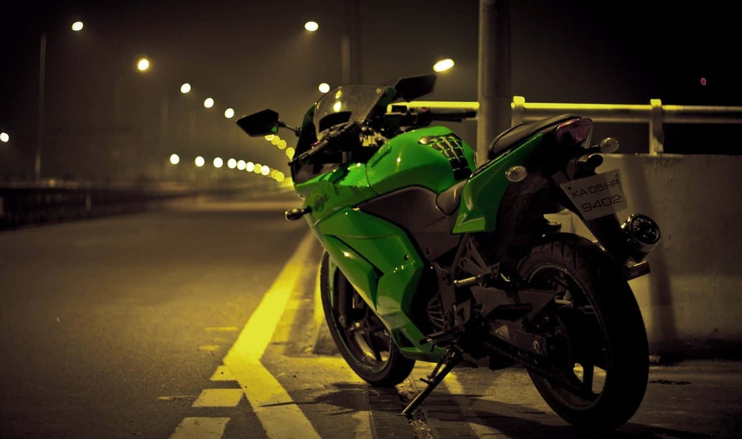 Kawasaki Desktop 桌布 壁紙 — 一台充滿活力的綠色機車停泊在霧氣瀰漫的夜晚街道上，被溫暖的黃色街燈照亮。