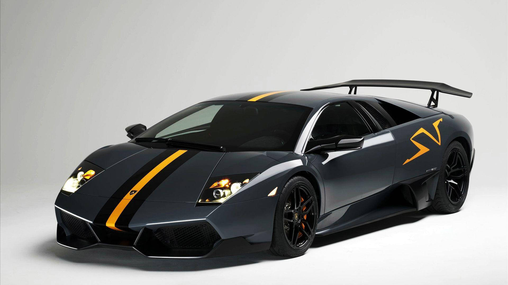 Lamborghini 4K 桌布 壁紙 — 一台型格啞黑色藍寶堅尼 Murciélago SV，帶有鮮明黃色賽車條紋和大型尾翼，在純白色攝影棚背景前展示。