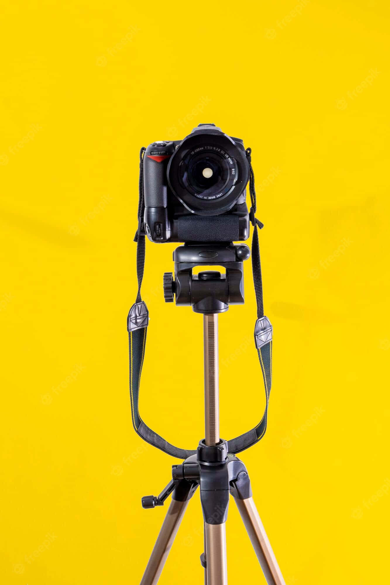 Dslr Camera 桌布 壁紙 — 一台安裝在三腳架上的黑色DSLR相機，在鮮黃色背景前居中擺放。
