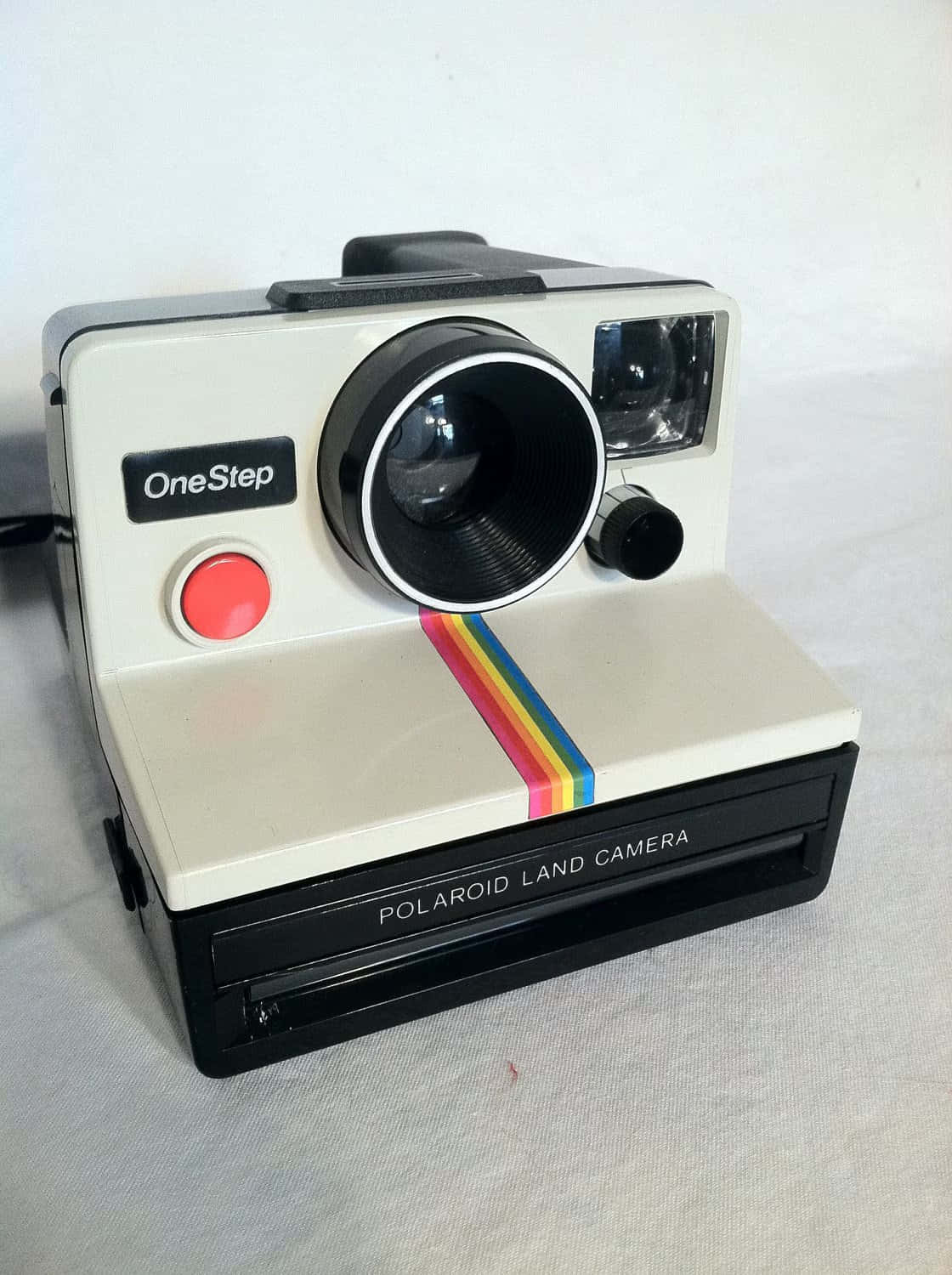 Polaroid 桌布 壁紙 — 一台帶有彩虹條紋的復古Polaroid OneStep Land相機放置在白色布料表面上。