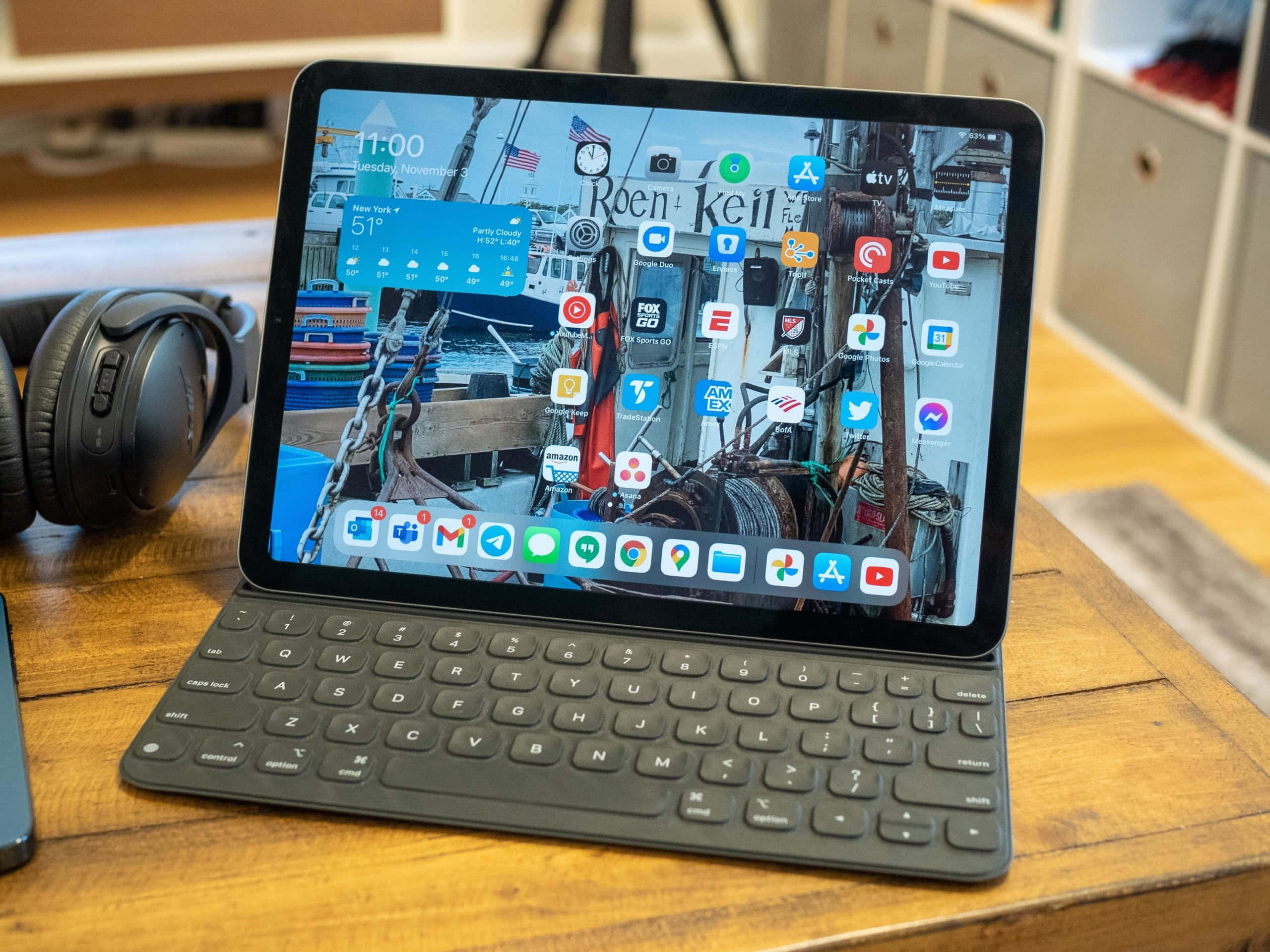 iPad 桌布 壁紙 — 一台帶有擴充基座鍵盤的平板電腦放在木桌上，旁邊有耳機，顯示帶有應用程式圖標的航海壁紙。
