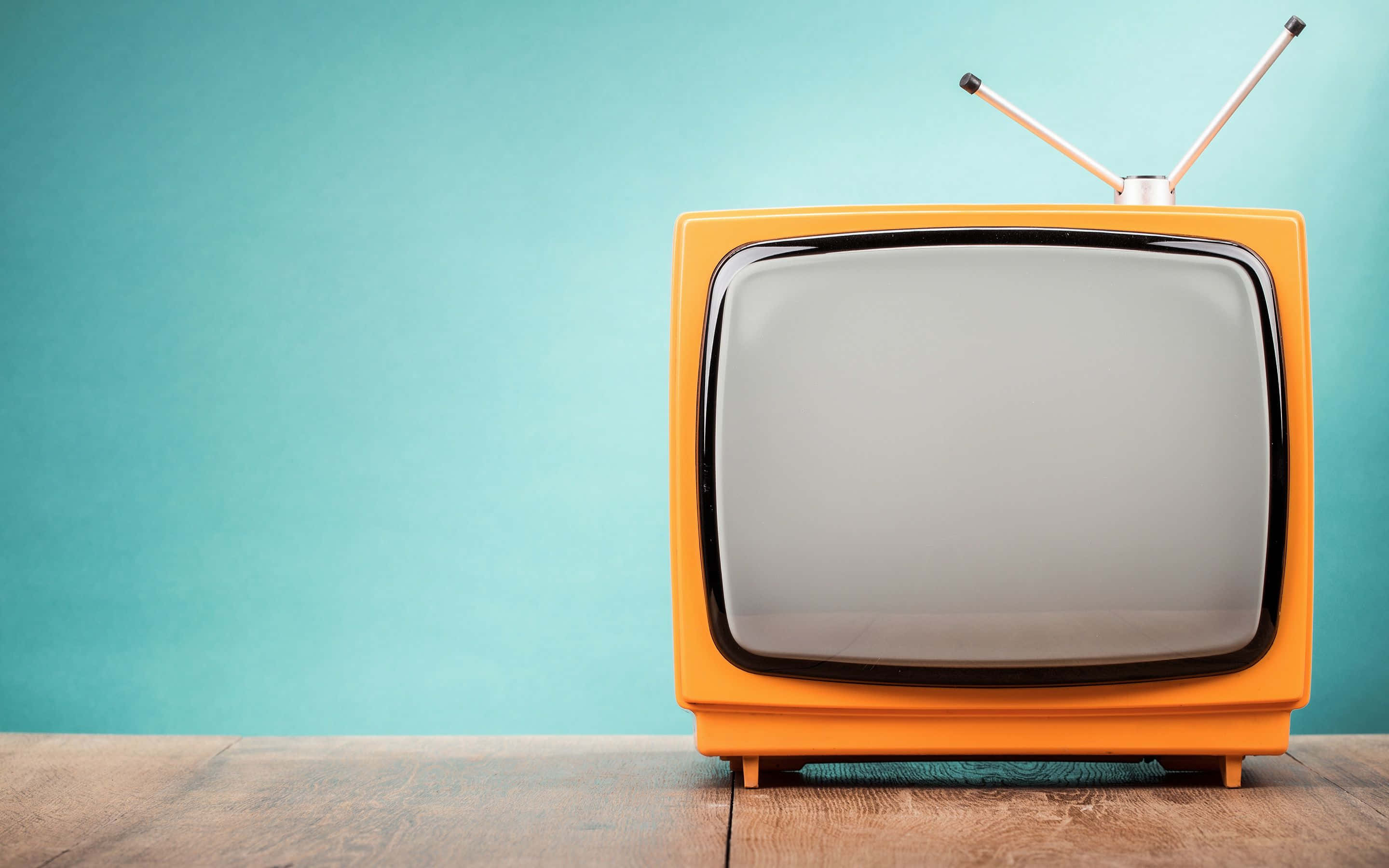 tv 桌布 壁紙 — 一台帶有鍍鉻天線的復古橙色電視機放在木質表面上，背景是青綠色牆壁。
