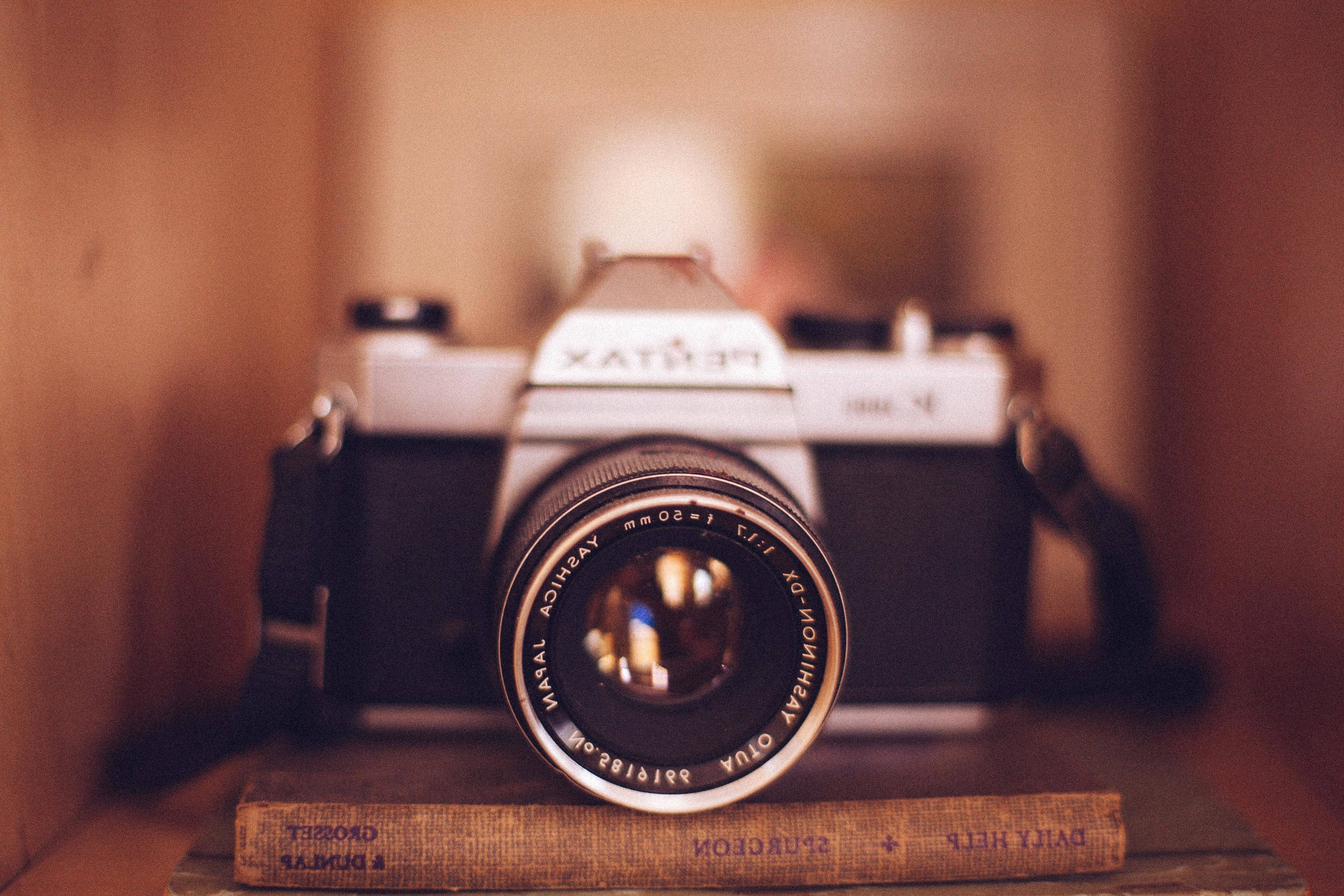 復古 桌布 壁紙 — 一台復古 Pentax 底片相機擱在舊書上，置於溫暖燈光的木架中，背景帶有柔和散景效果。