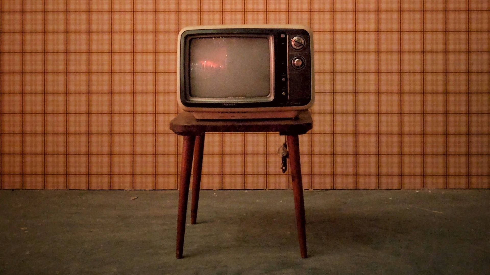 tv 桌布 壁紙 — 一台復古CRT電視獨自放在木凳上，背景是格子壁紙，房間燈光昏暗。