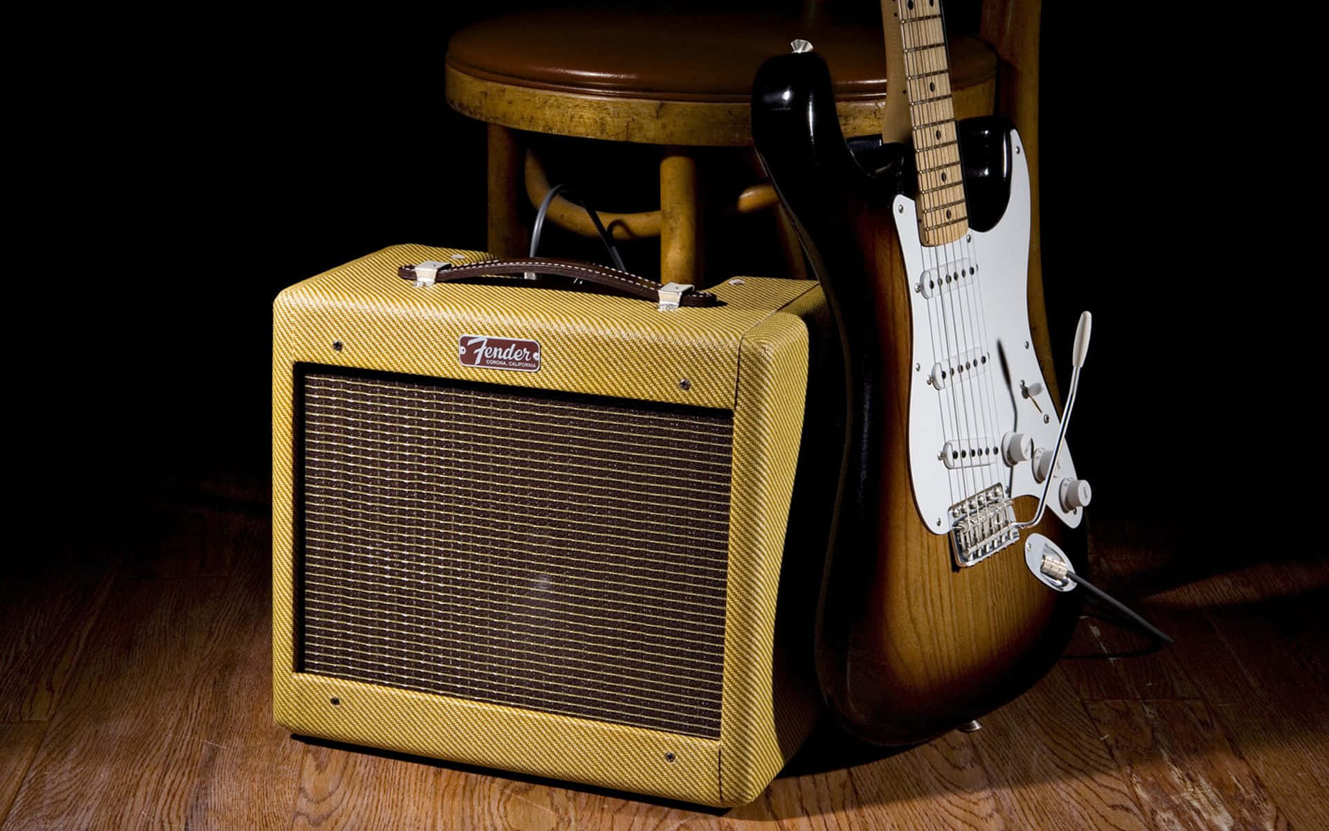 Guitar Amp 桌布 壁紙 — 一台復古Fender吉他音箱和一把旭日色電吉他放在昏暗錄音室的木地板上，旁邊有一張凳子。