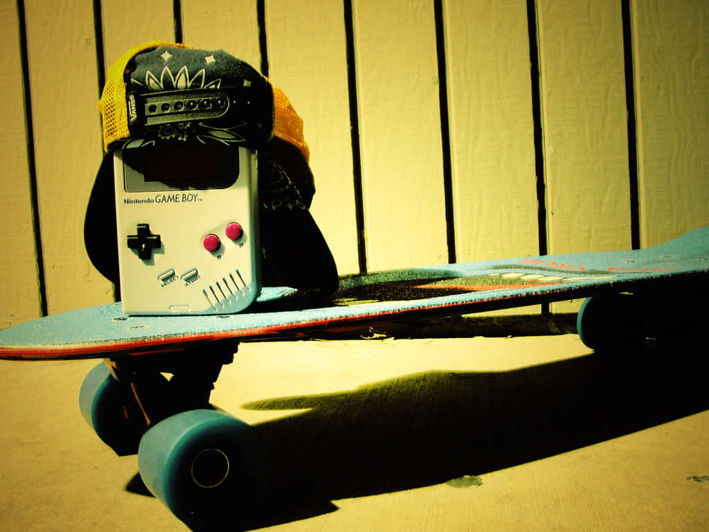 Retro Skateboard 桌布 壁紙 — 一台復古Game Boy戴著頭巾，放在長板滑板上，靠著木柵欄，在溫暖的黃光下。