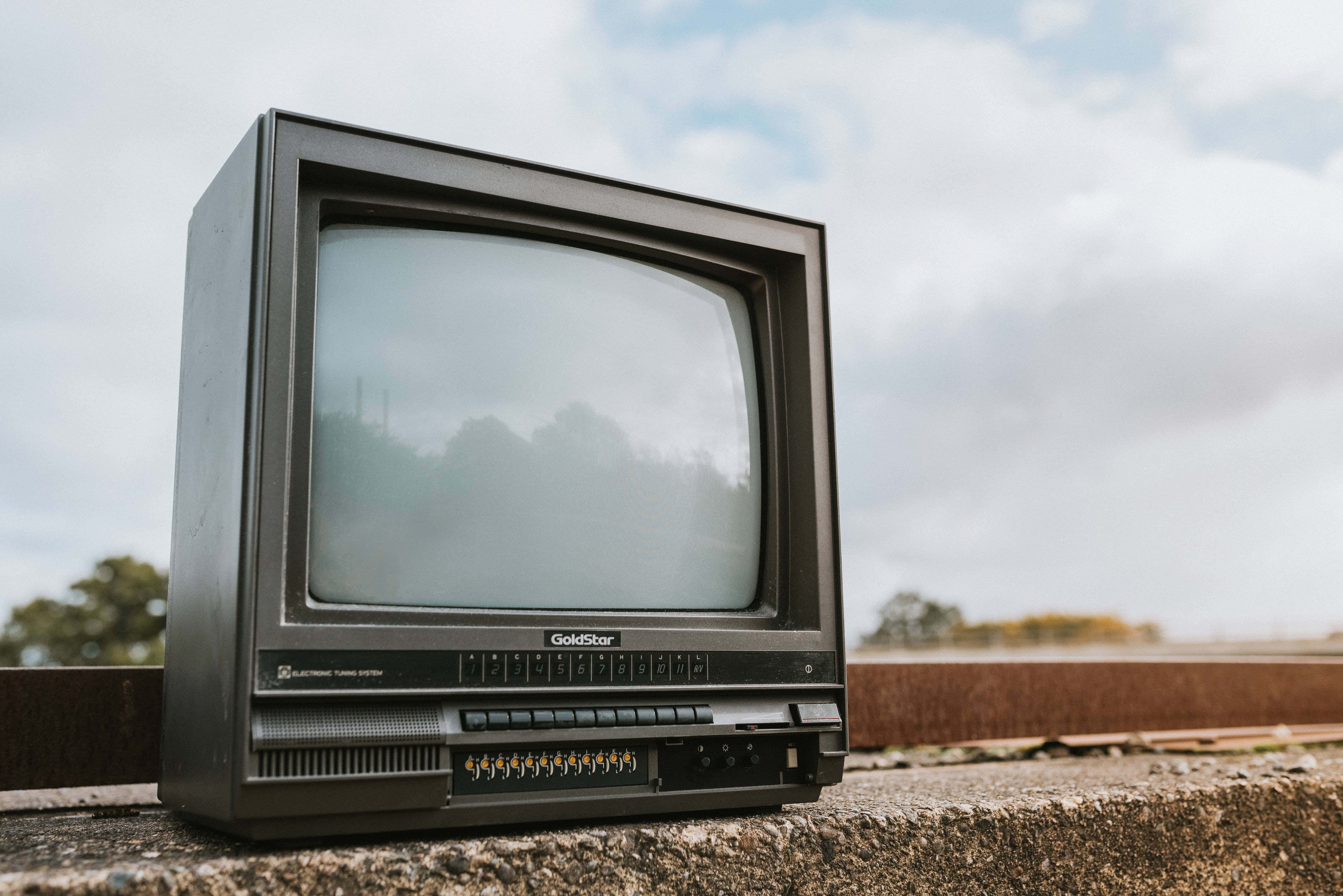 television 桌布 壁紙 — 一台復古GoldStar CRT電視被遺棄在混凝土簷上，天空多雲，螢幕反射出樹木。