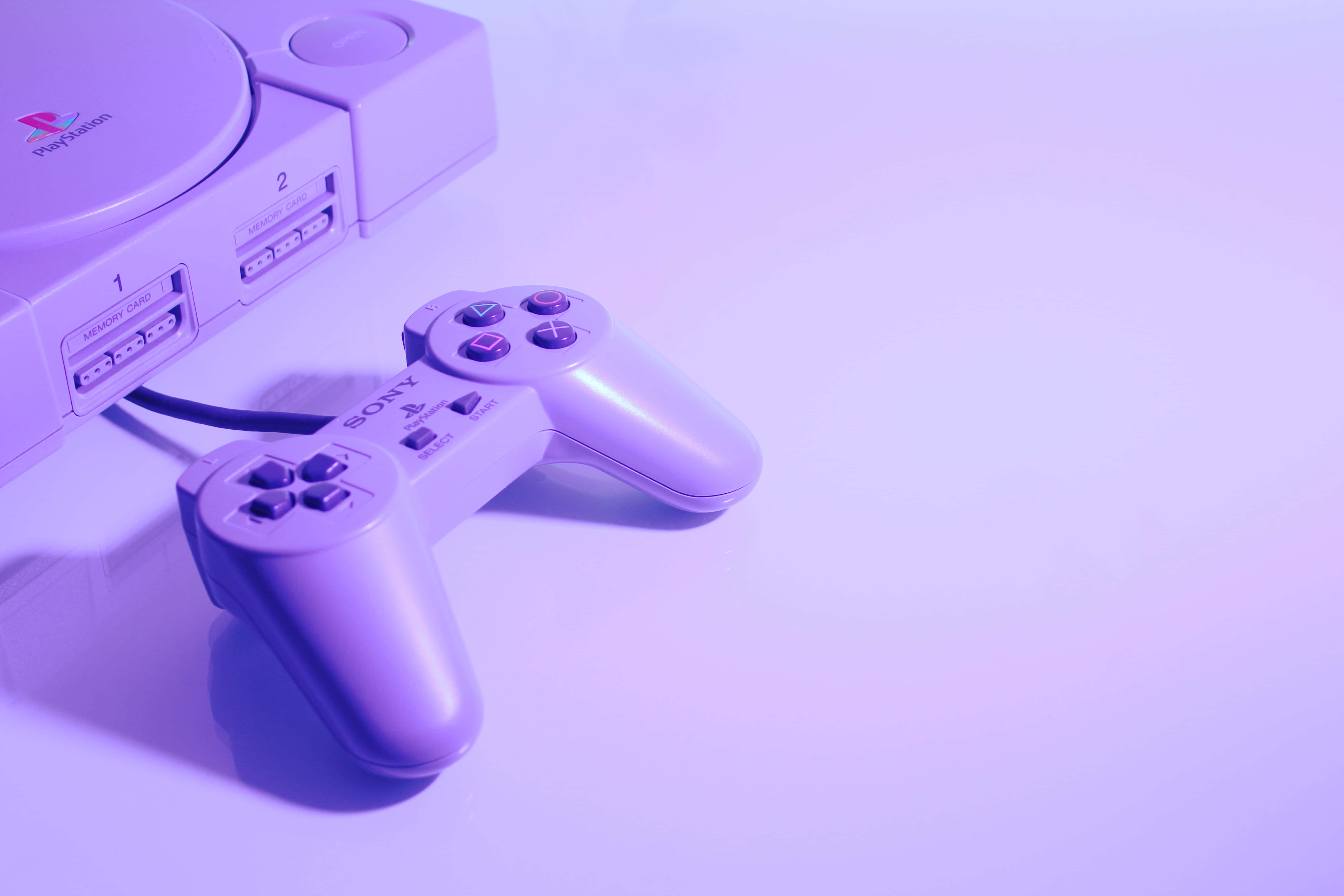 Gaming Consoles 桌布 壁紙 — 一台復古PlayStation主機和手把，沐浴在柔和的紫色燈光下，置於簡約的白色表面上。