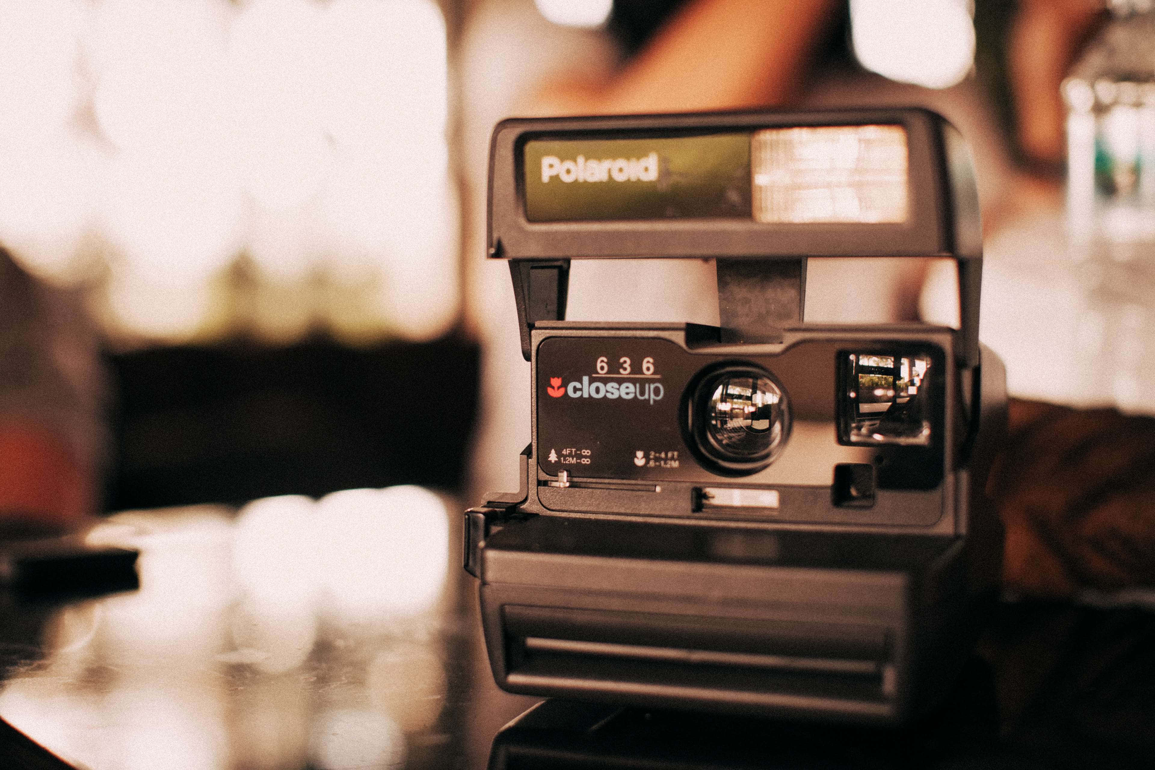Polaroid Camera 桌布 壁紙 — 一台復古Polaroid 636 Closeup相機放在反射表面上，沐浴在溫暖的金色光線中，背景柔和模糊。