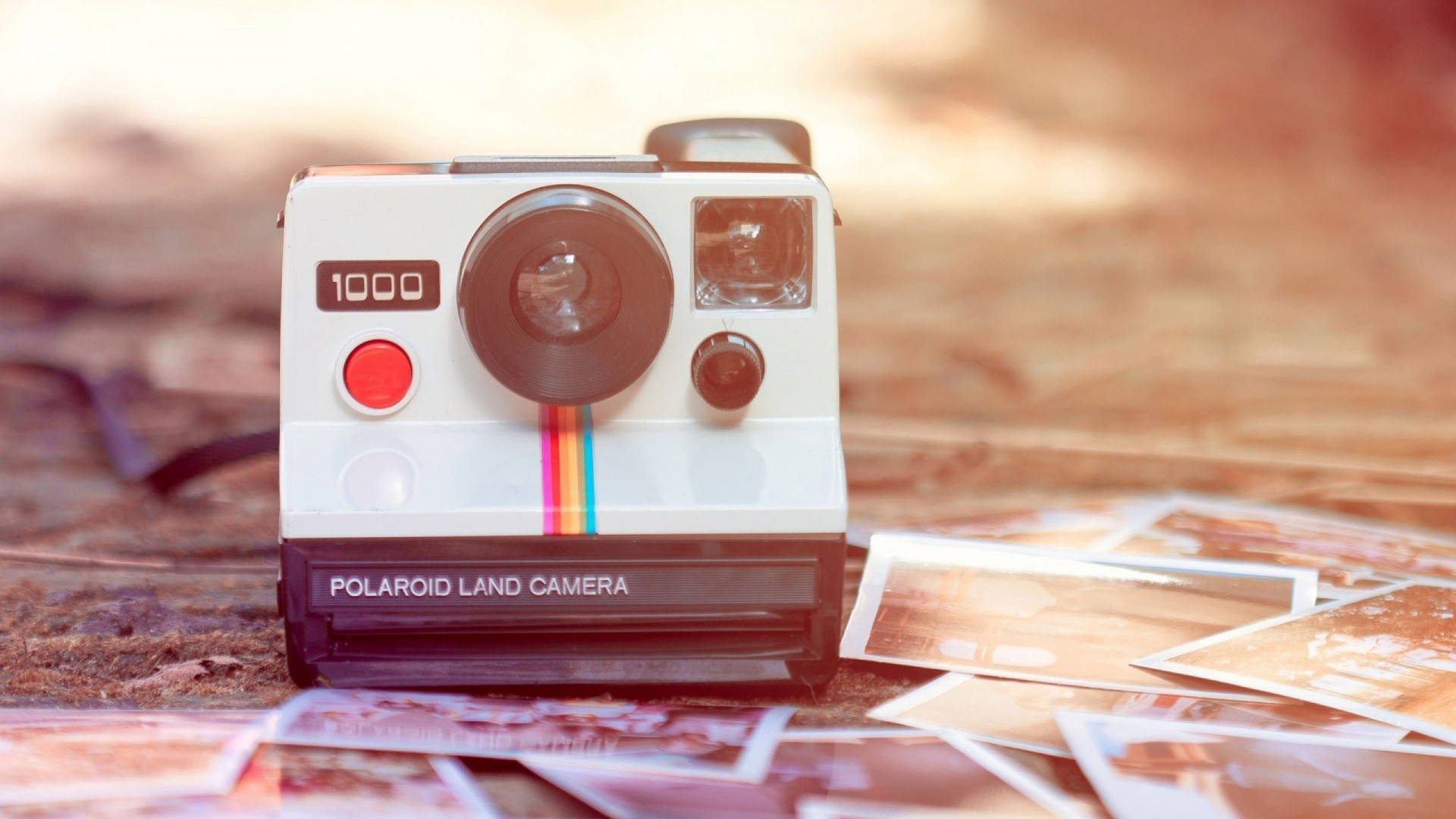 拍立得 桌布 壁紙 — 一台復古Polaroid Land Camera 1000放在木質表面上，周圍散落著即時照片，沐浴在溫暖的金色光線中。