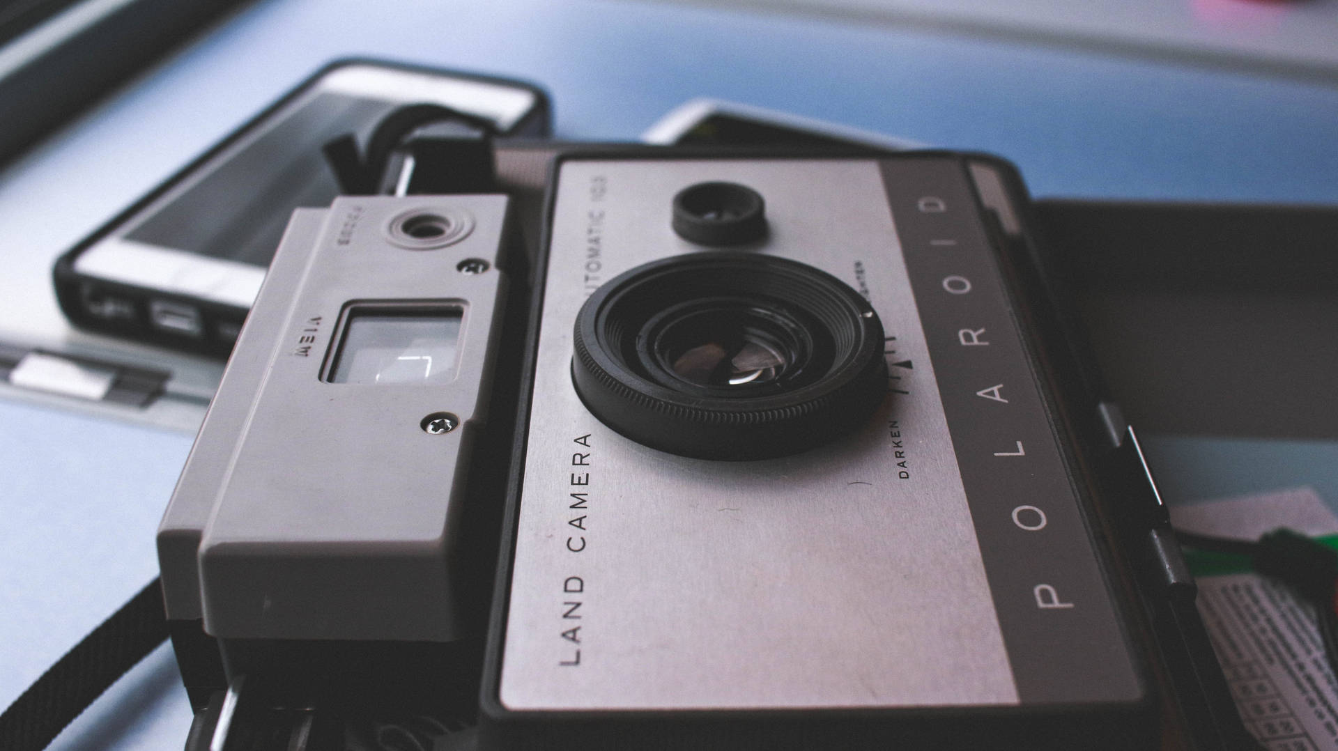 復古Polaroid相機放在藍色桌子上的智慧型手機旁邊。