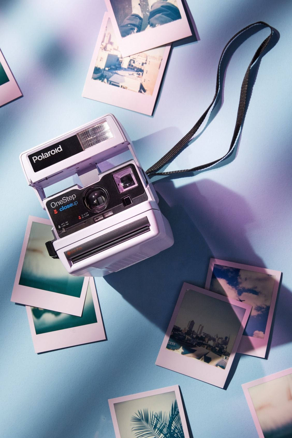 Retro 桌布 壁紙 — 一台復古Polaroid OneStep相機放在藍色表面上，周圍散落著沐浴在柔和紫色光線中的即時照片。