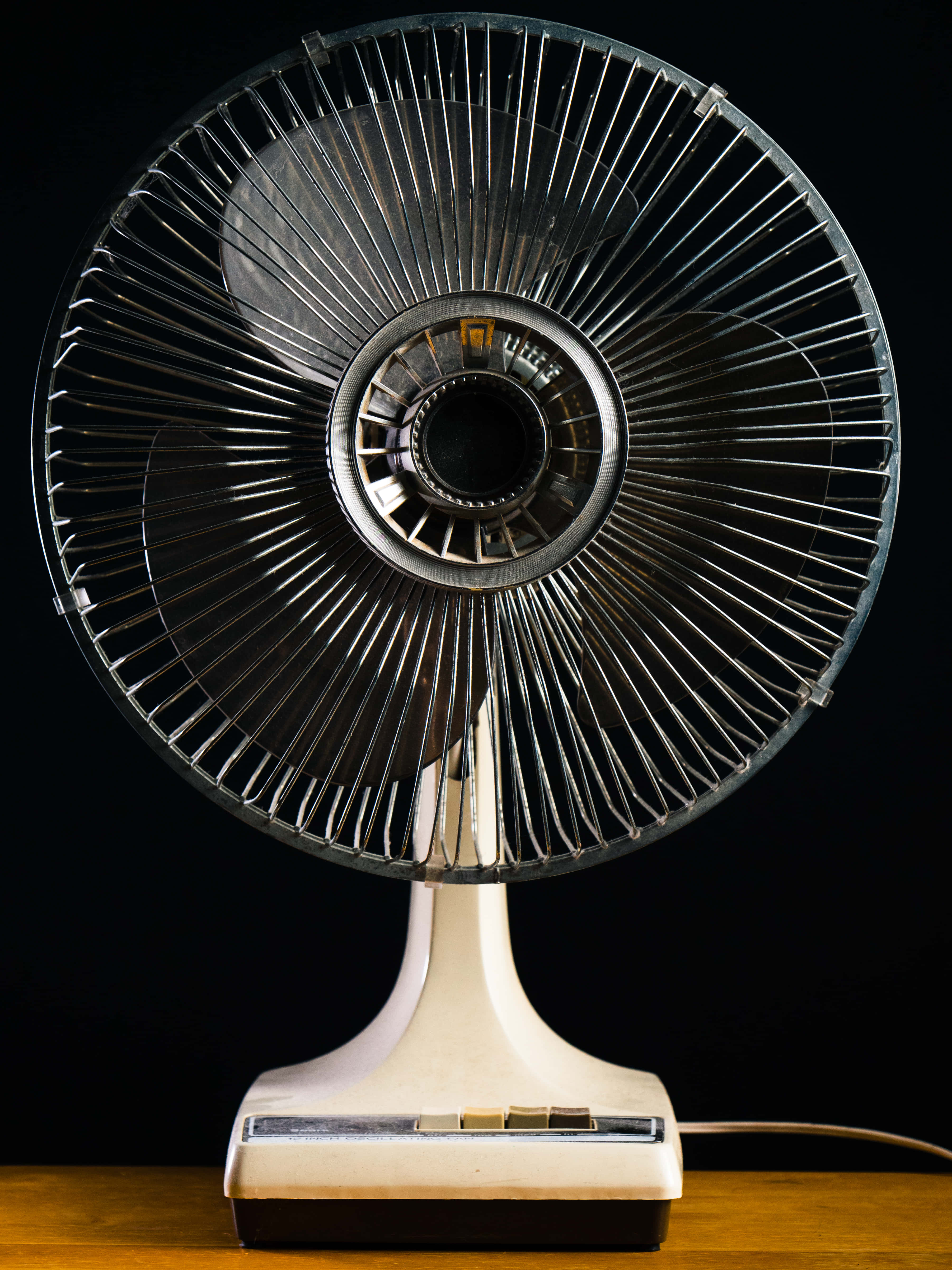 fan 桌布 壁紙 — 一台復古奶油色立式風扇，帶金屬網罩，立於黑色背景前的木質表面上。
