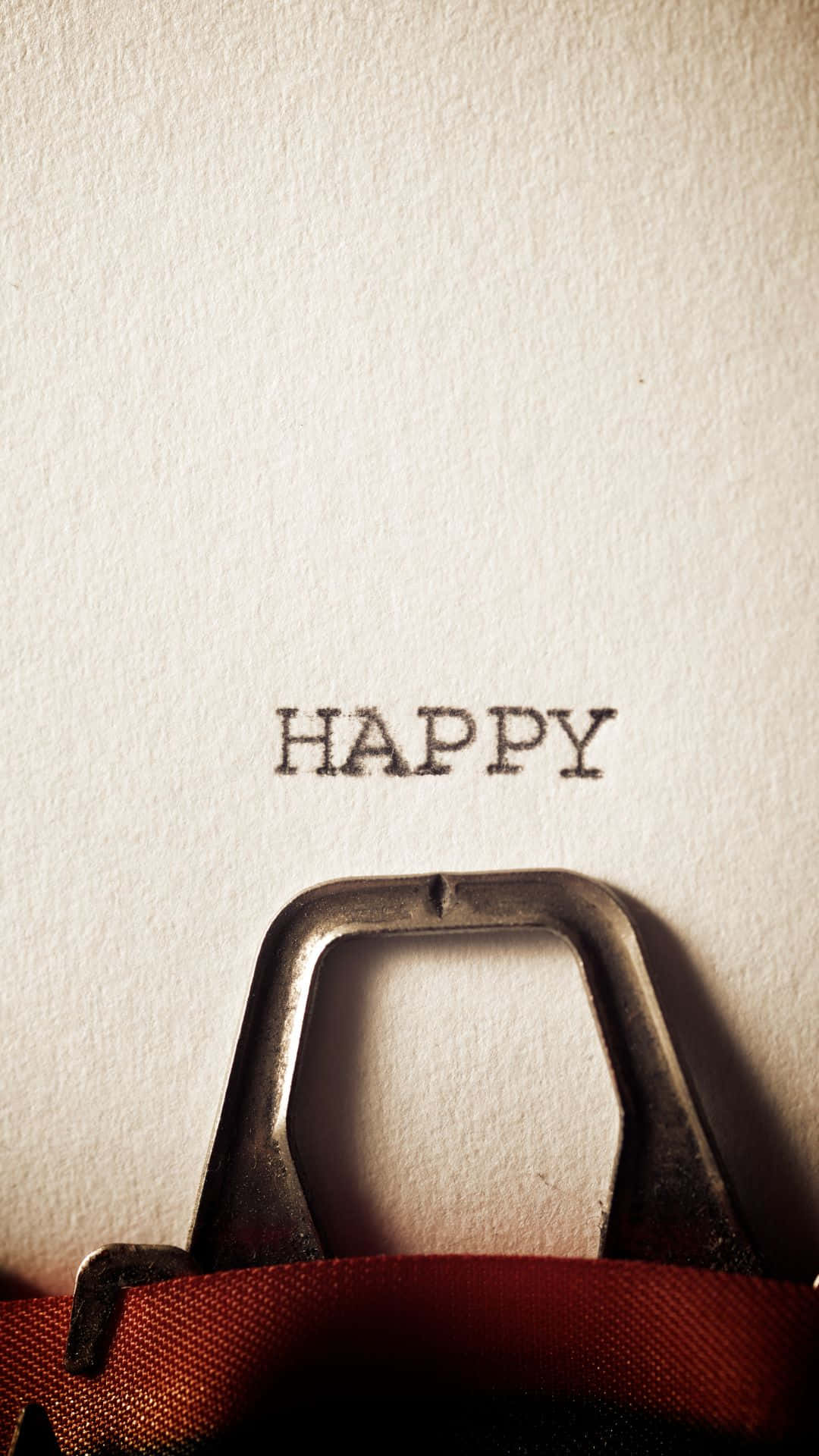 Happy iPhone 桌布 壁紙 — 一台復古打字機的按鍵在溫暖燈光下將「happy」一詞壓印在帶紋理的奶油色紙上。