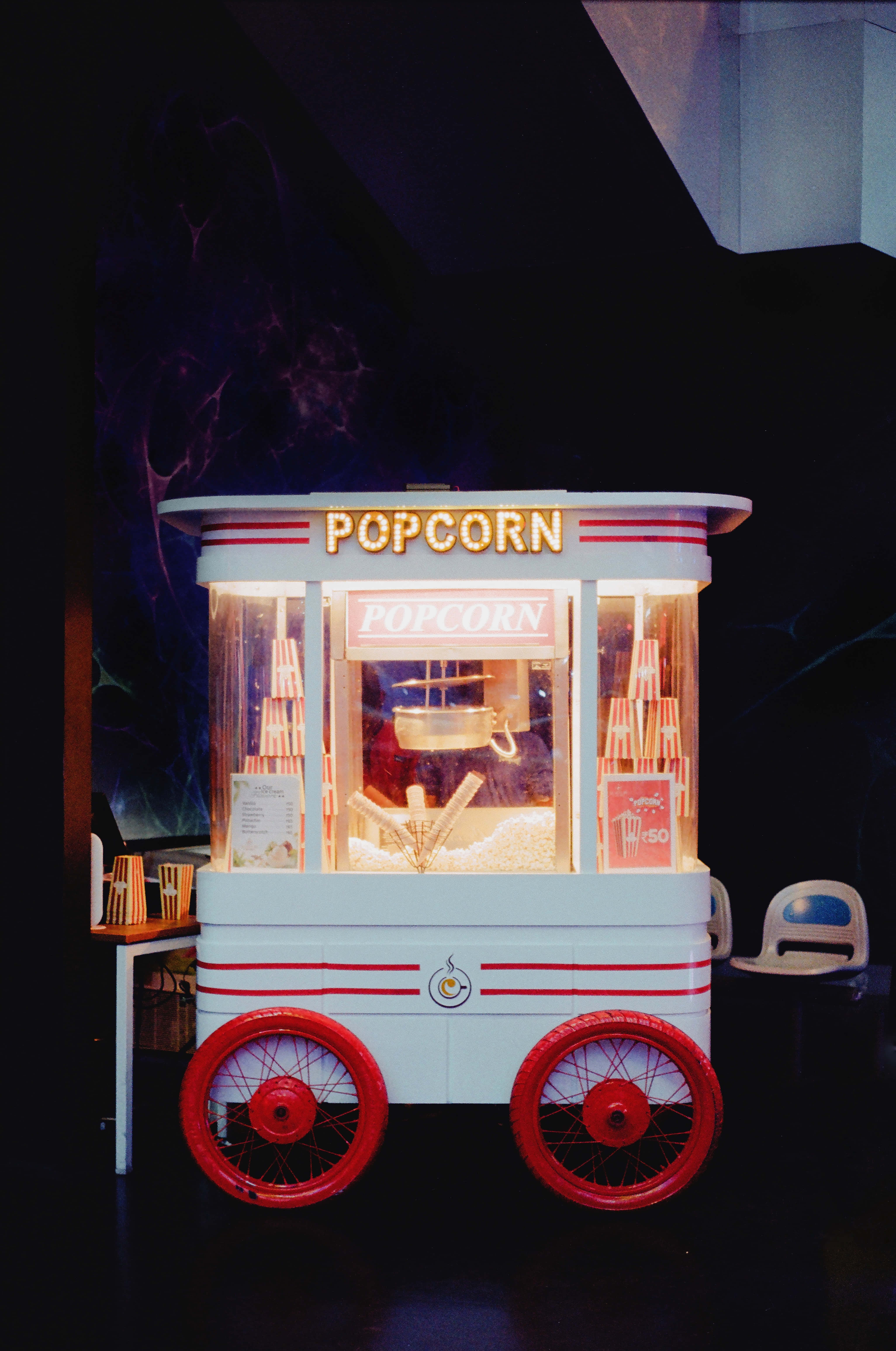Popcorn 桌布 壁紙 — 一台復古白色爆米花車，配有紅色車輪和發光霓虹招牌，在黑暗背景下被照亮。