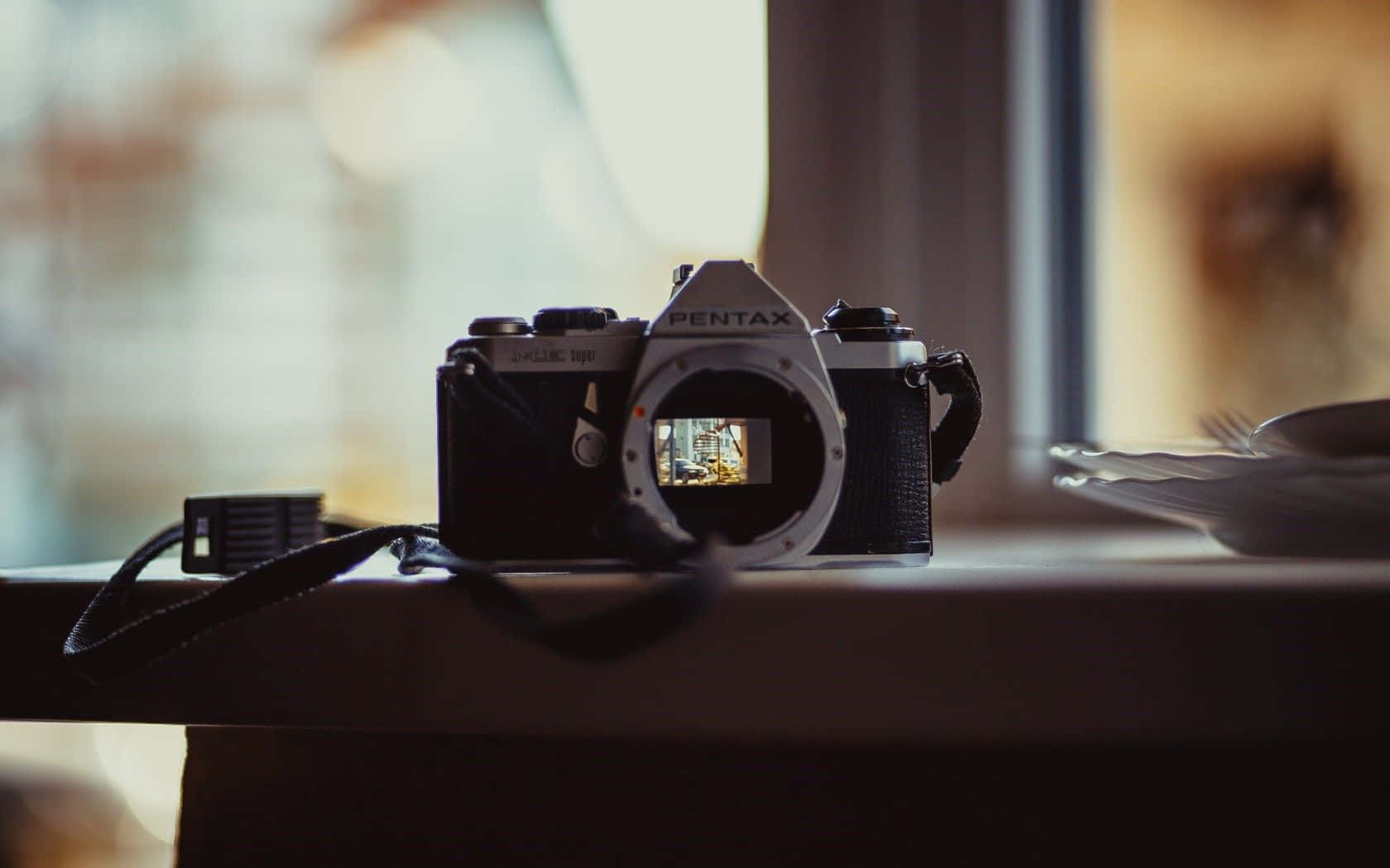Photography Desktop 桌布 壁紙 — 一台復古的Pentax底片相機放在窗台上，鏡頭蓋打開，露出溫暖的散景背景。