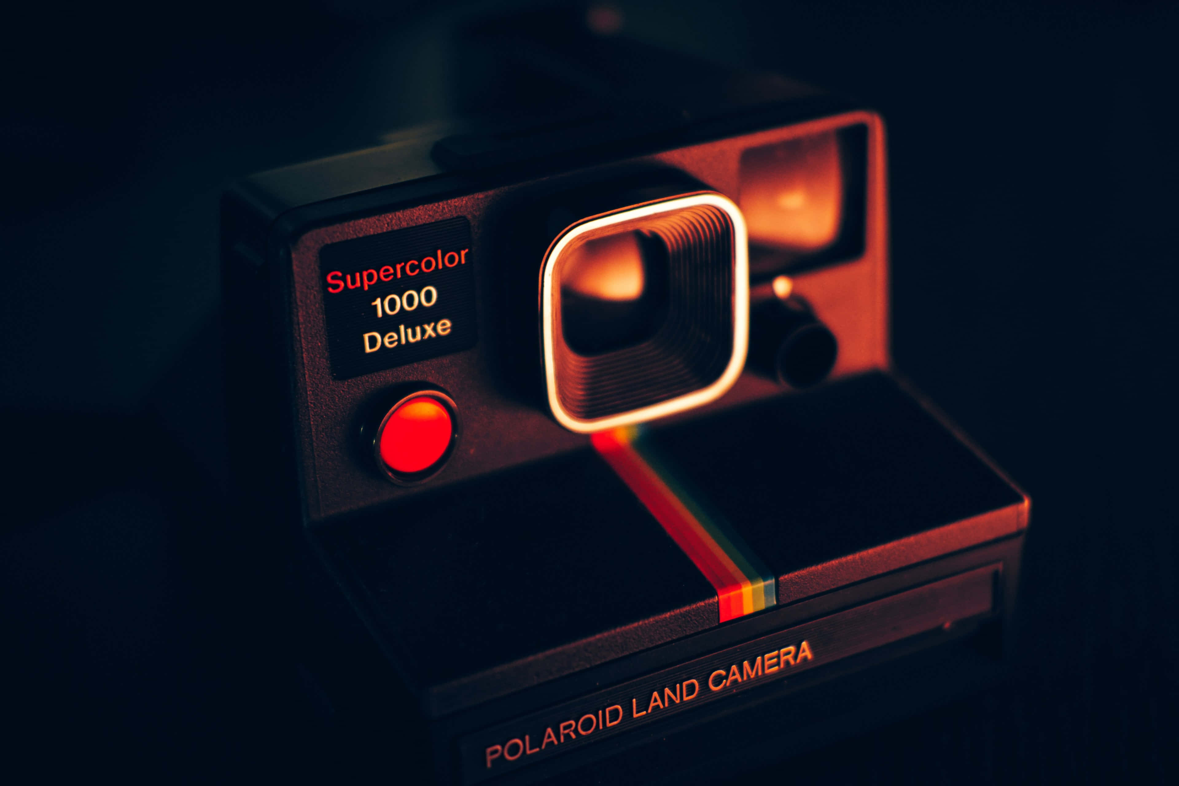 Vintage Camera 桌布 壁紙 — 一台復古的Polaroid Land Camera SuperColor 1000 Deluxe在黑暗背景下發出溫暖的紅光。