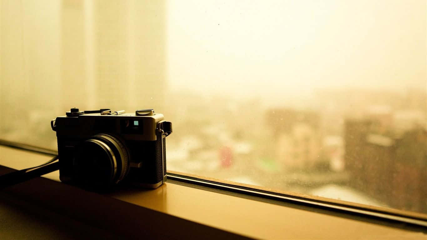 Photography Desktop 桌布 壁紙 — 一台復古相機放在窗台上，俯瞰著沐浴在溫暖金色光芒中的朦朧城市景觀。