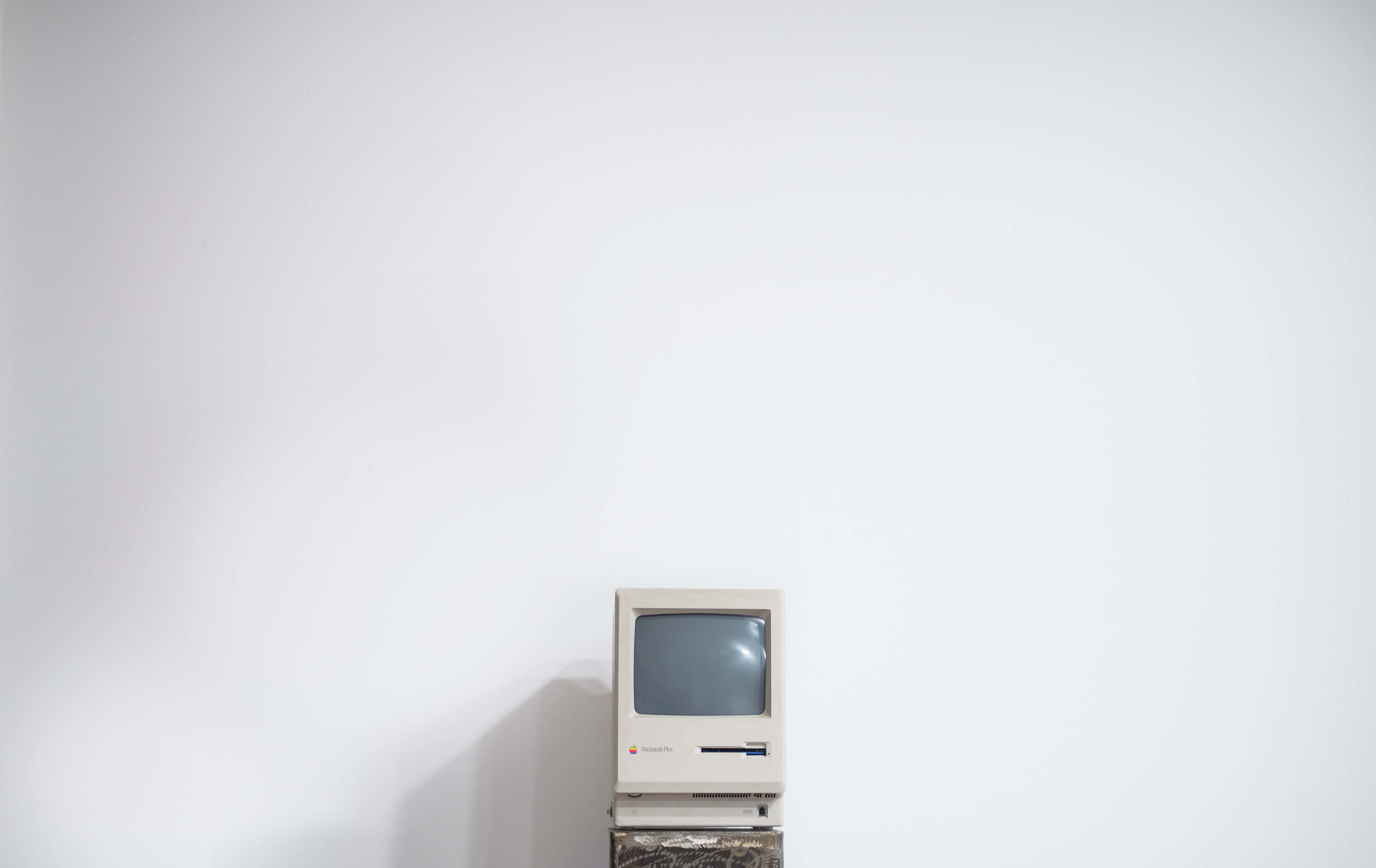 Minimalist Vintage 桌布 壁紙 — 一台復古米色 Apple Macintosh 電腦獨自放在木製支架上，背景是純白牆壁。