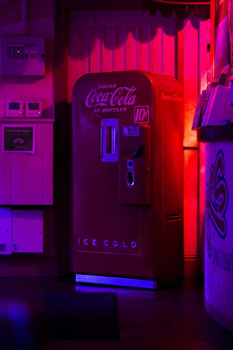 coca cola 桌布 壁紙 — 一台復古紅色可口可樂自動販賣機在昏暗的復古遊戲機中心內，在霓虹粉紅和藍色燈光下發光。