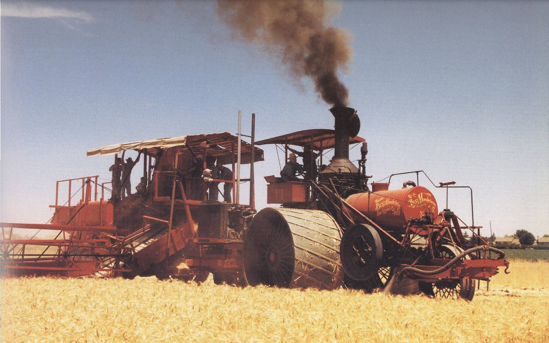 Tractor 桌布 壁紙 — 一台復古紅色蒸汽驅動收割機在晴朗藍天下收割金色小麥，煙囪冒著滾滾濃煙。