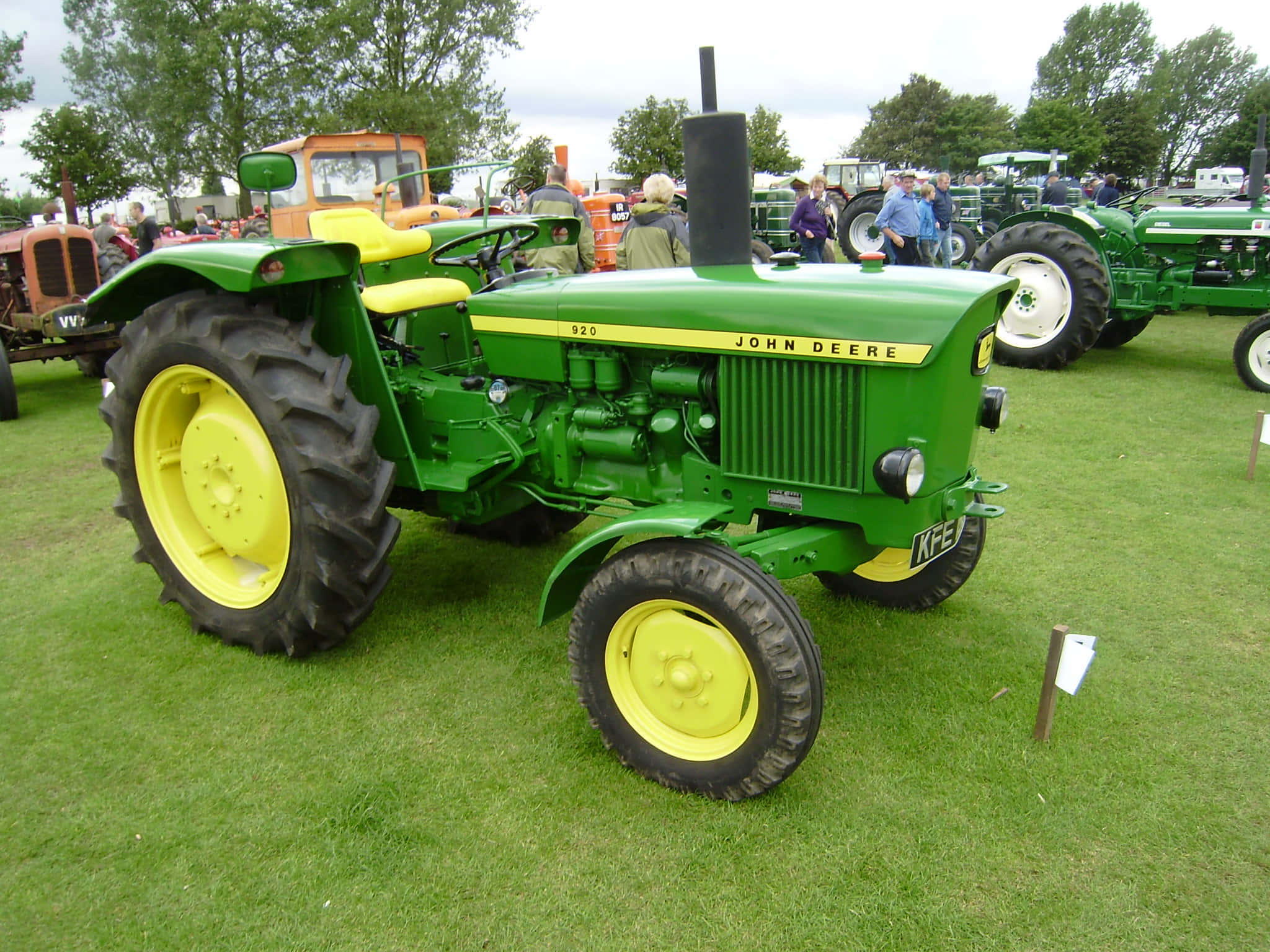 Tractor 桌布 壁紙 — 一台復古綠色和黃色的約翰迪爾拖拉機，配有大黑色輪胎，在戶外農業展覽的草地上顯眼地停放。