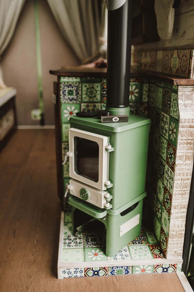 Stove 桌布 壁紙 — 一台復古綠色柴火爐，帶白色飾邊，放置在鋪有花卉瓷磚的舒適鄉村風格房間內，地板為木質。