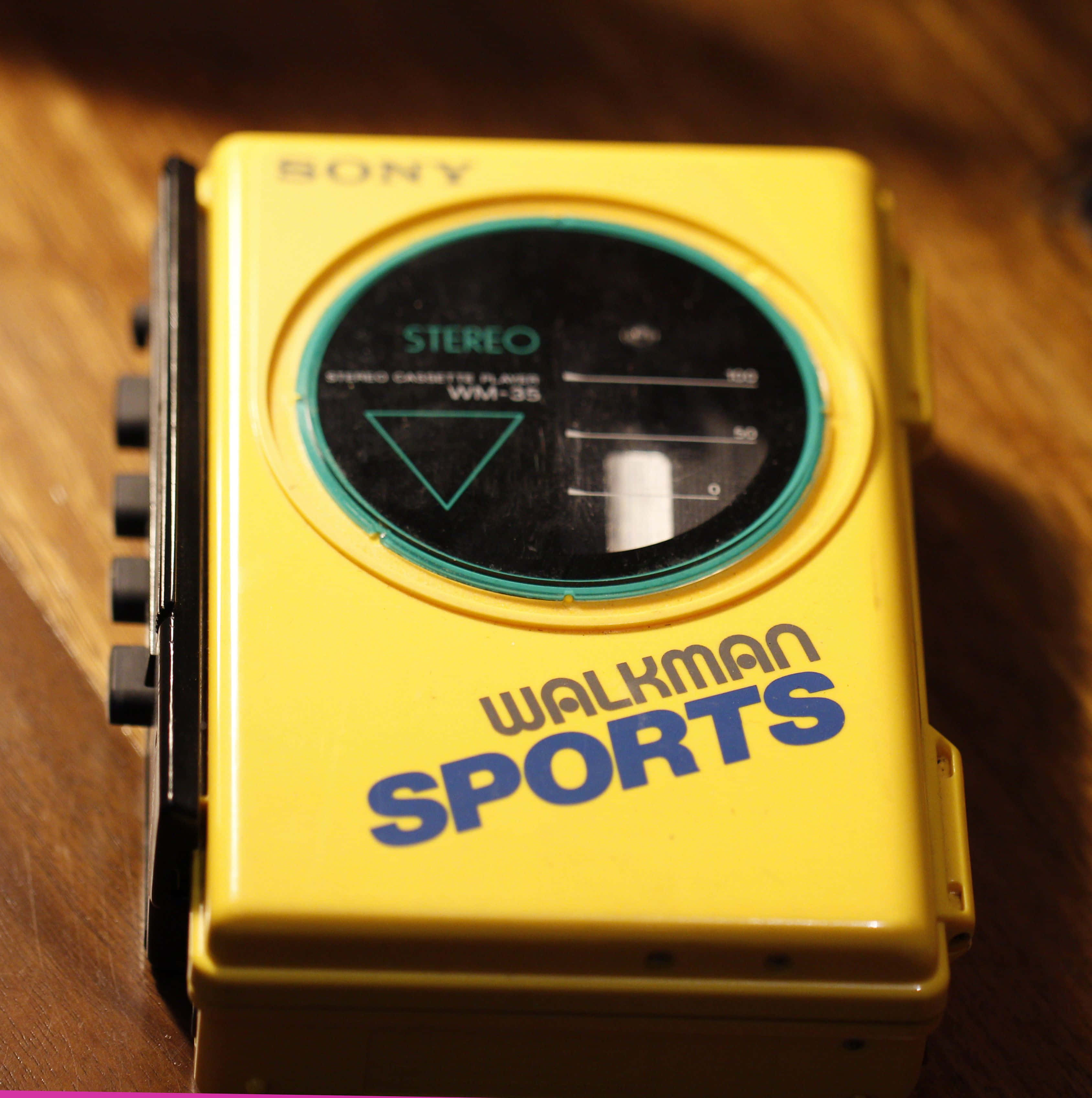 1980s 桌布 壁紙 — 一台復古黃色Sony Walkman Sports WM-35卡式錄音機放在木質表面上，在溫暖燈光下。