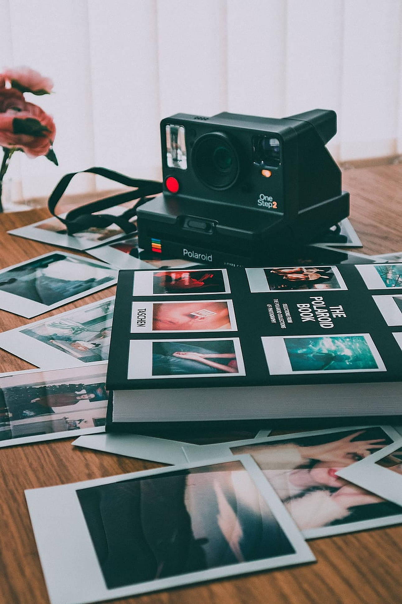 拍立得 桌布 壁紙 — 一台復古黑色Polaroid One Step 2相機放在一本書上，周圍散落著即時照片在木桌上。
