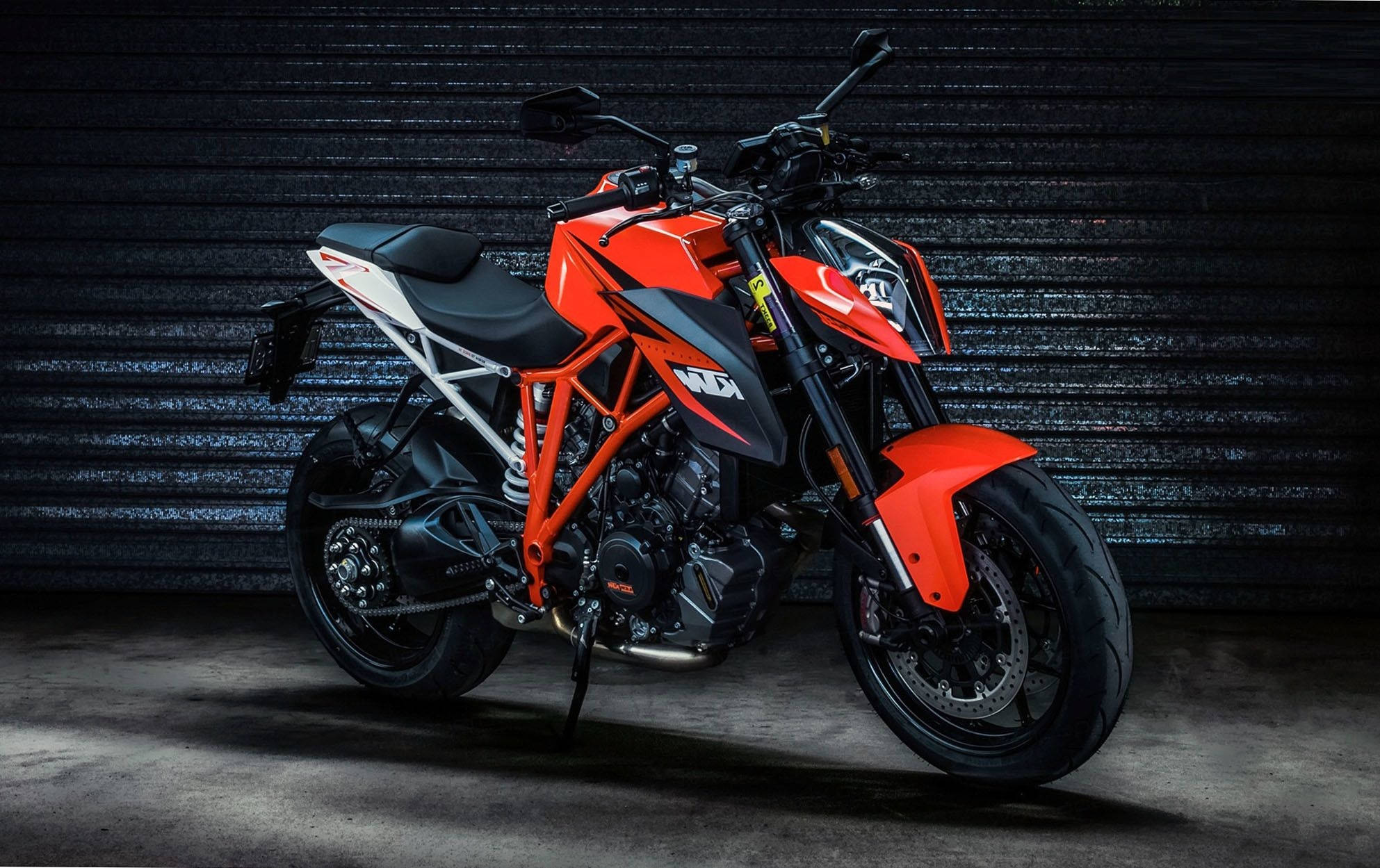 Ktm Bike 桌布 壁紙 — 一台搶眼的橙色和黑色KTM機車，在昏暗的工業車庫中，以深色波紋金屬牆為背景，蓄勢待發。