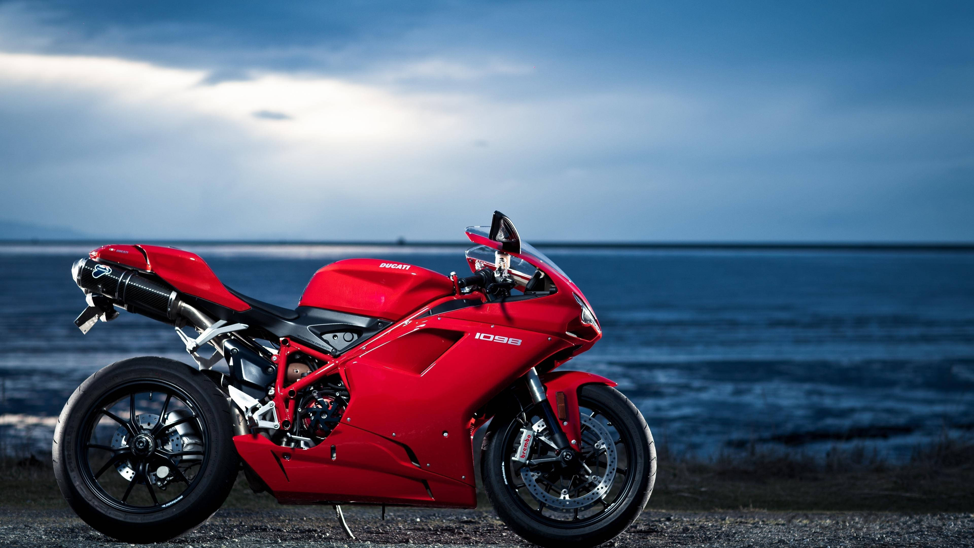 4K bike 桌布 壁紙 — 一台搶眼的紅色Ducati 1098重機，在暮色海洋和密雲天空的背景下，佇立在碎石岸邊。