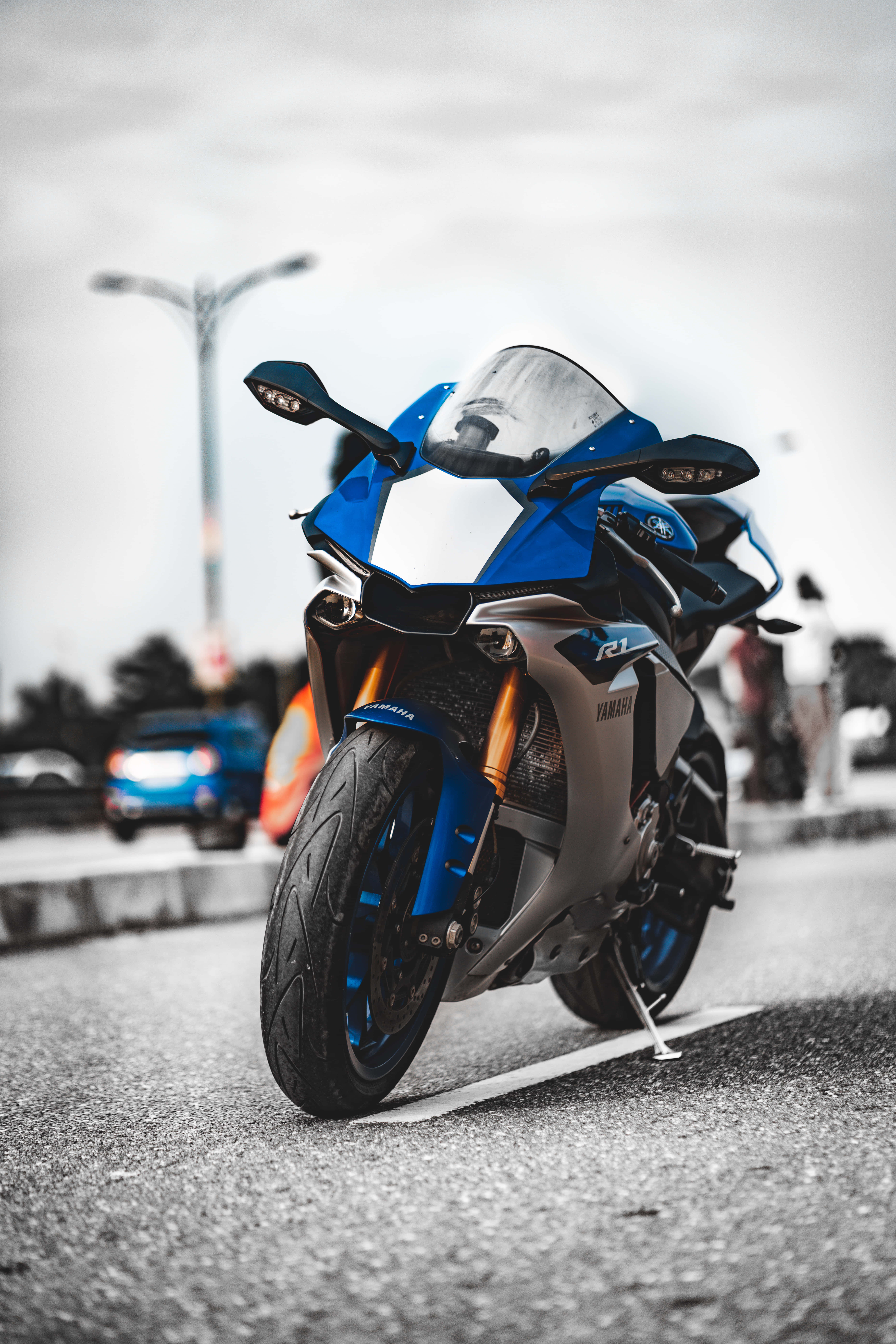 桌布 壁紙 — 一台搶眼的藍色Yamaha R1重型機車停放在柏油路上，背景是模糊的城市景觀。