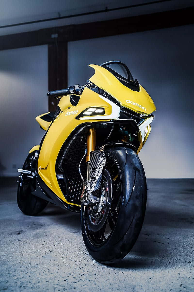 Electric Bike 桌布 壁紙 — 一台搶眼的黃色Damon機車，配備金色前叉和黑色飾件，在極簡混凝土車庫中，於戲劇性燈光下蓄勢待發。