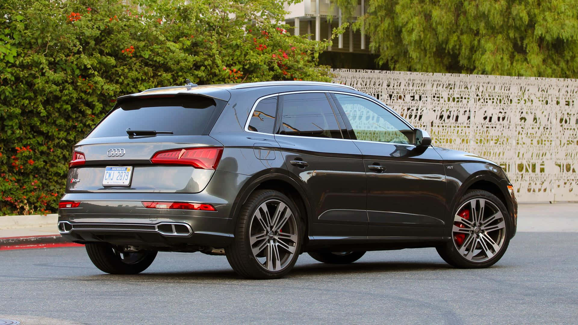 Audi Sq5 桌布 壁紙 — 一台時尚灰色奧迪Q5 SUV停在柏油路上，透過合金輪圈可見紅色煞車卡鉗，周圍環繞綠色灌木叢和白色裝飾圍欄。