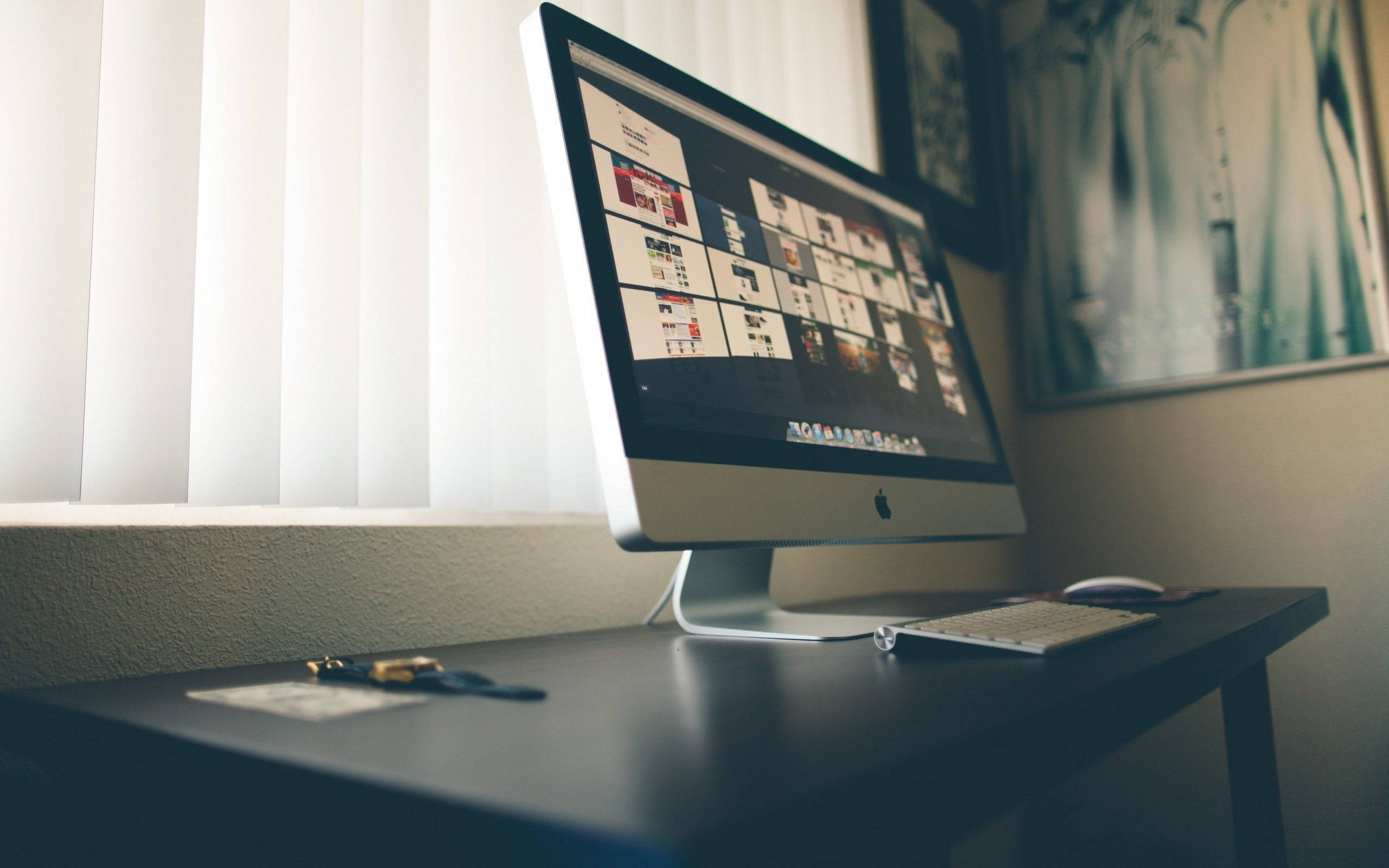 Desk 桌布 壁紙 — 一台時尚的iMac在深色桌子上顯示網站模擬圖的網格，旁邊有百葉窗和裱框藝術品。