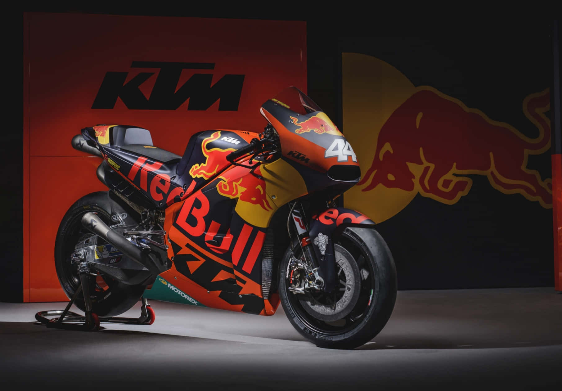 機車 桌布 壁紙 — 一台時尚的KTM MotoGP摩托車搭配Red Bull塗裝，在工作室場景中矗立於品牌背景前。