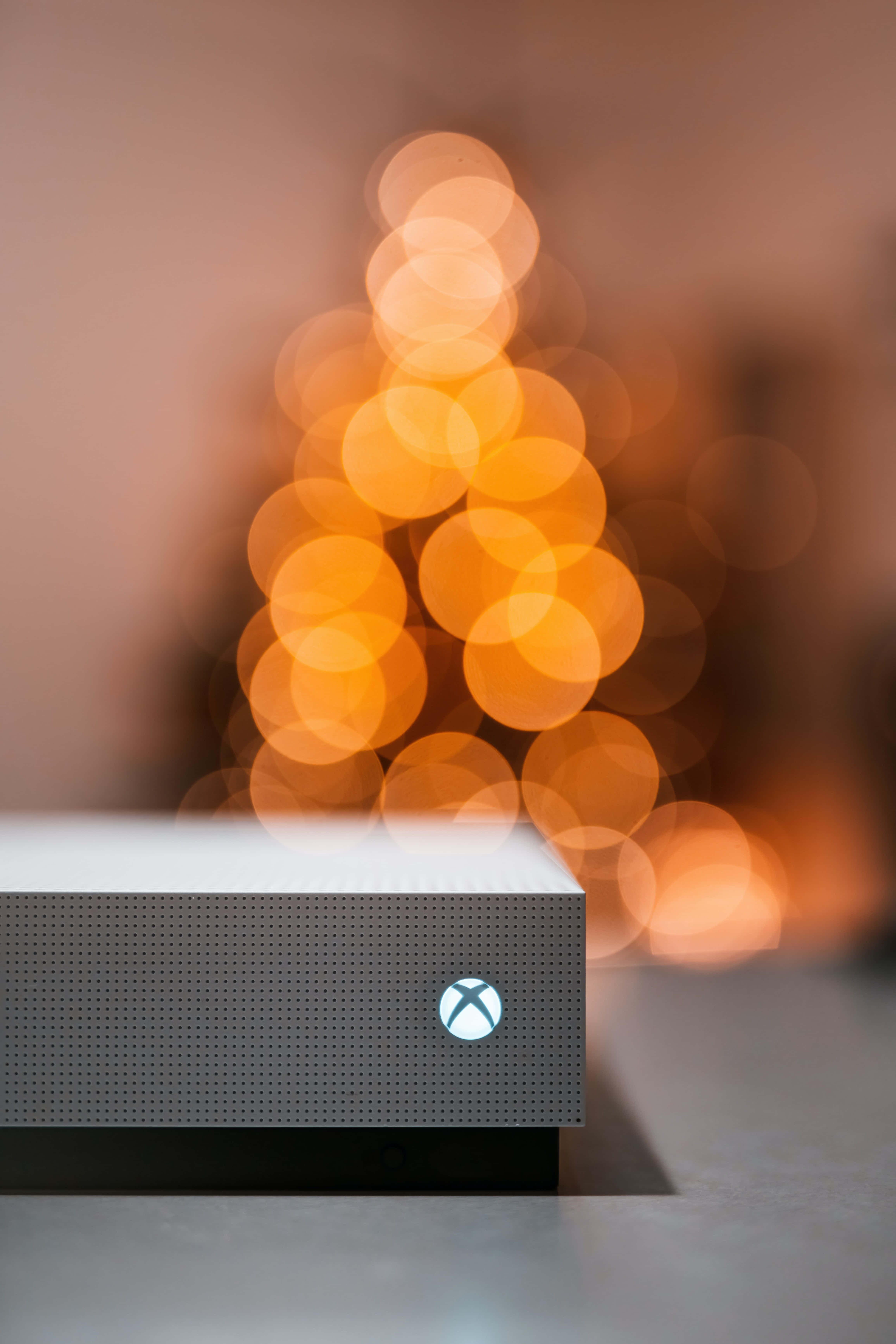 Gaming Consoles 桌布 壁紙 — 一台時尚的Xbox主機位於前景，背後有溫暖的散景聖誕樹柔和地發光。