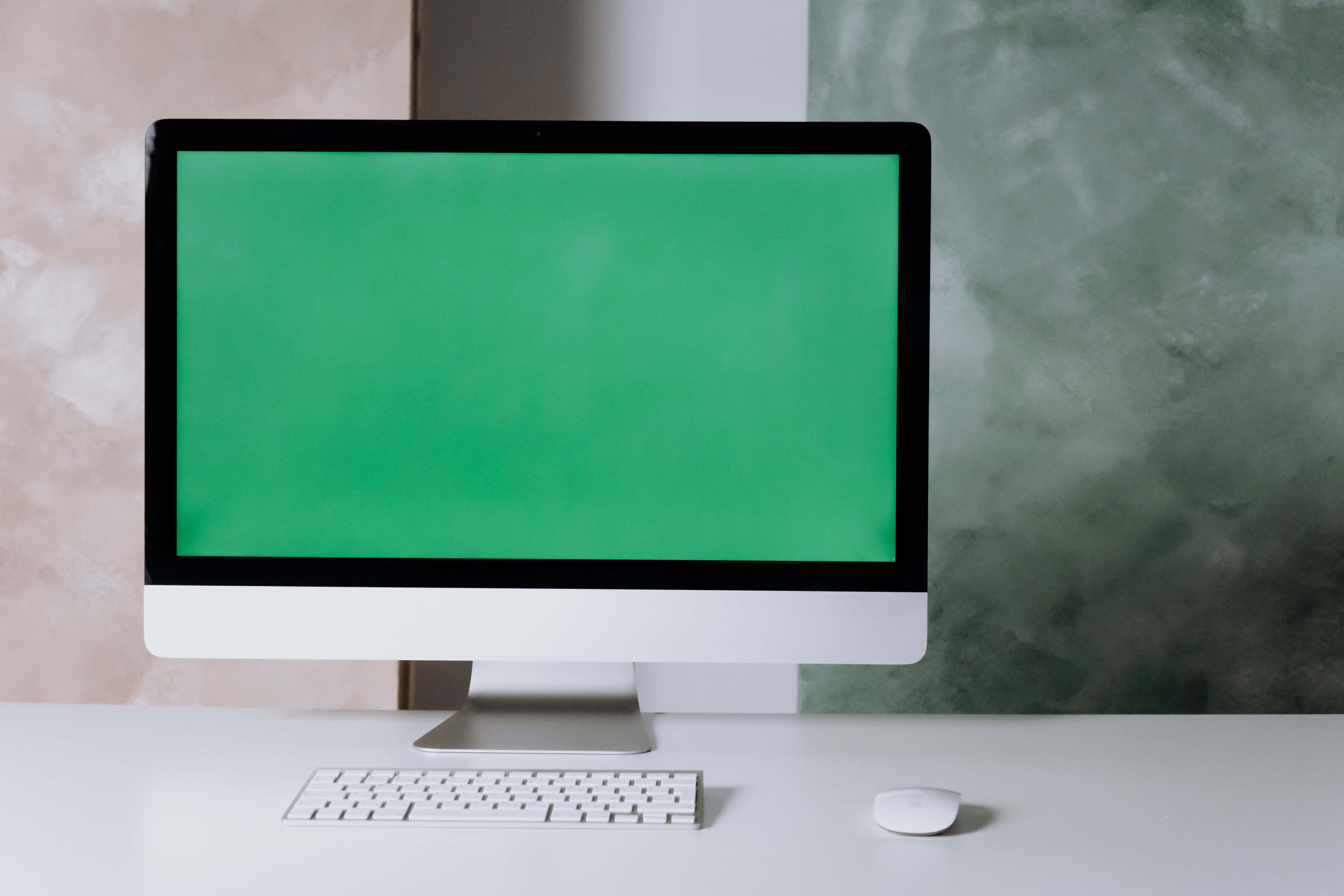 Green Screen 桌布 壁紙 — 一台時尚的一體式電腦配備綠色螢幕，放置在白色桌子上，旁邊有鍵盤和滑鼠，背景是帶有紋理的牆壁。