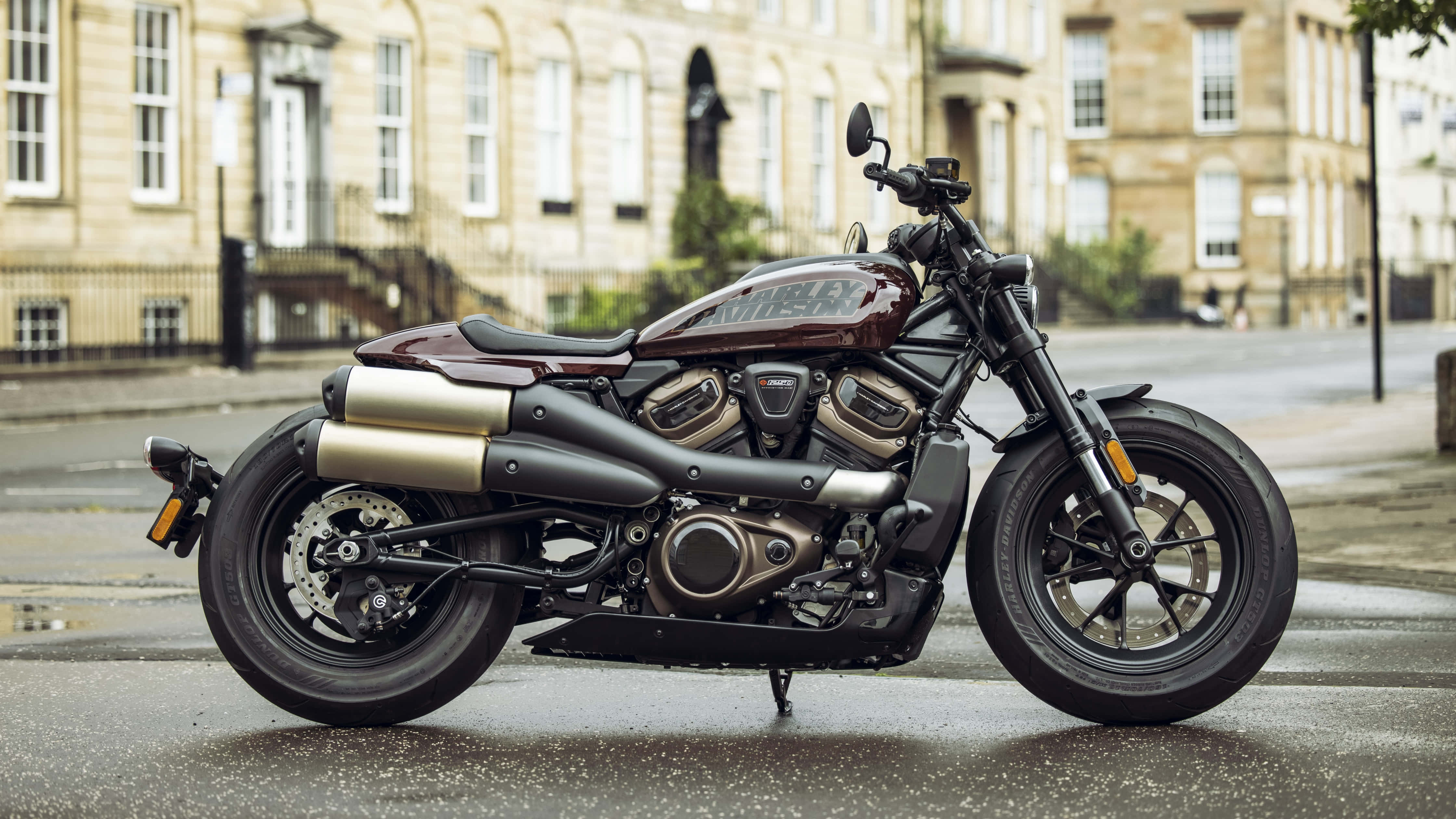 Harley Davidson HD 桌布 壁紙 — 一台時尚的栗色和鍍鉻Harley-Davidson摩托車停放在潮濕的城市街道上，背景是歷史悠久的石造建築。