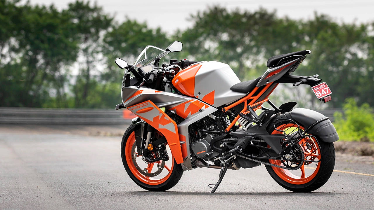KTM RC 200 桌布 壁紙 — 一台時尚的橙色和銀色KTM運動機車停在柏油路上，背景有綠樹。
