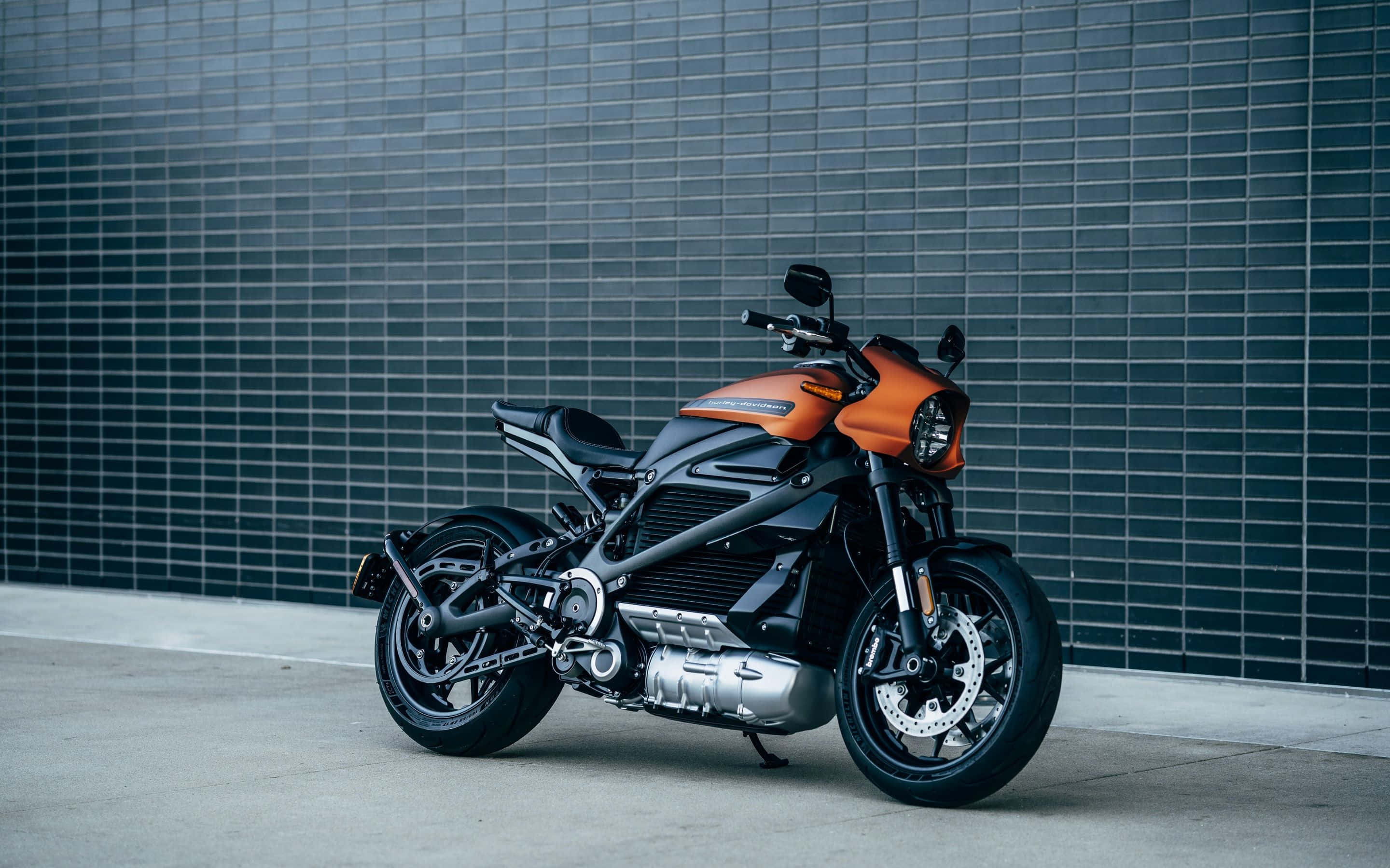 Electric Bike 桌布 壁紙 — 一台時尚的橙色和黑色電動機車，在混凝土表面上靠著深色瓷磚牆擺好姿勢。