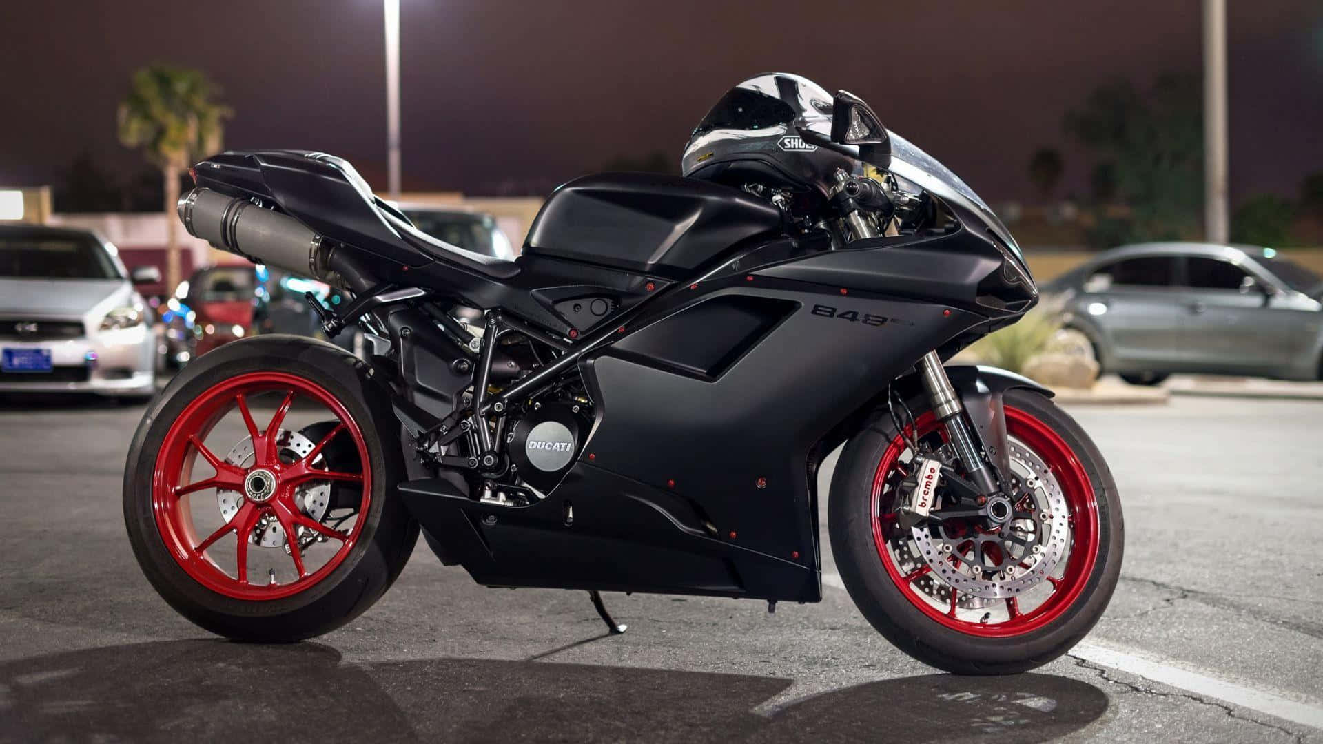 腳踏車 桌布 壁紙 — 一台時尚的消光黑色Ducati摩托車，搭配鮮紅色輪圈，夜晚停在燈光明亮的停車場。