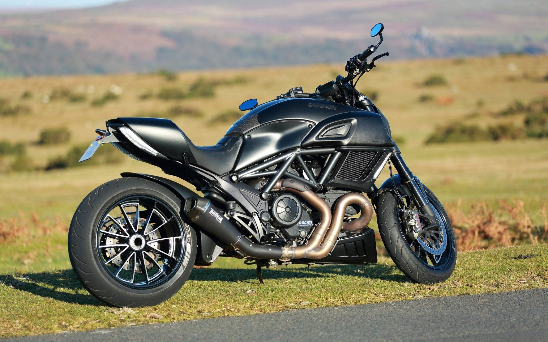 Cool Bike 桌布 壁紙 — 一台時尚的消光黑色Ducati機車停在路邊的草地上，背景是綿延起伏的山丘。