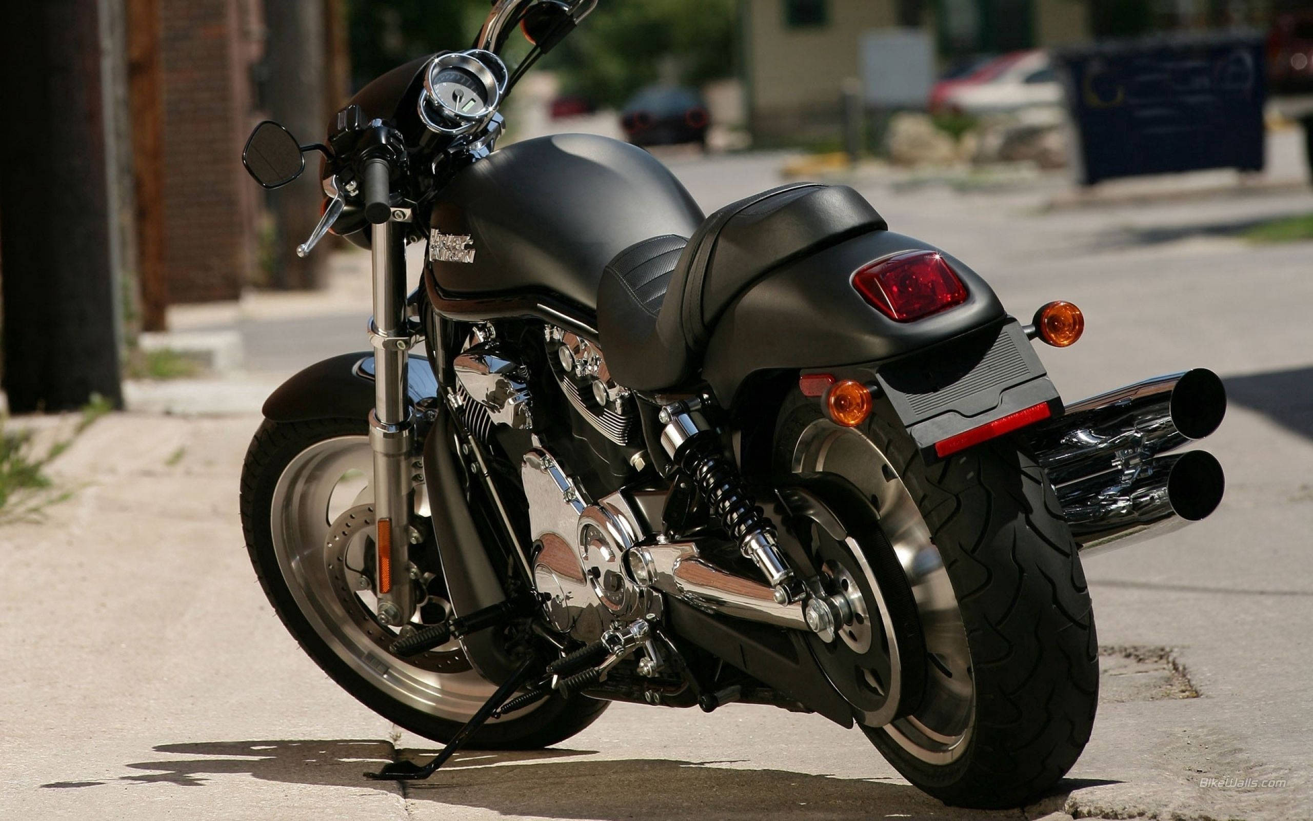 Harley 桌布 壁紙 — 一台時尚的消光黑色機車，帶有鍍鉻裝飾，停放在陽光普照的城市人行道上。