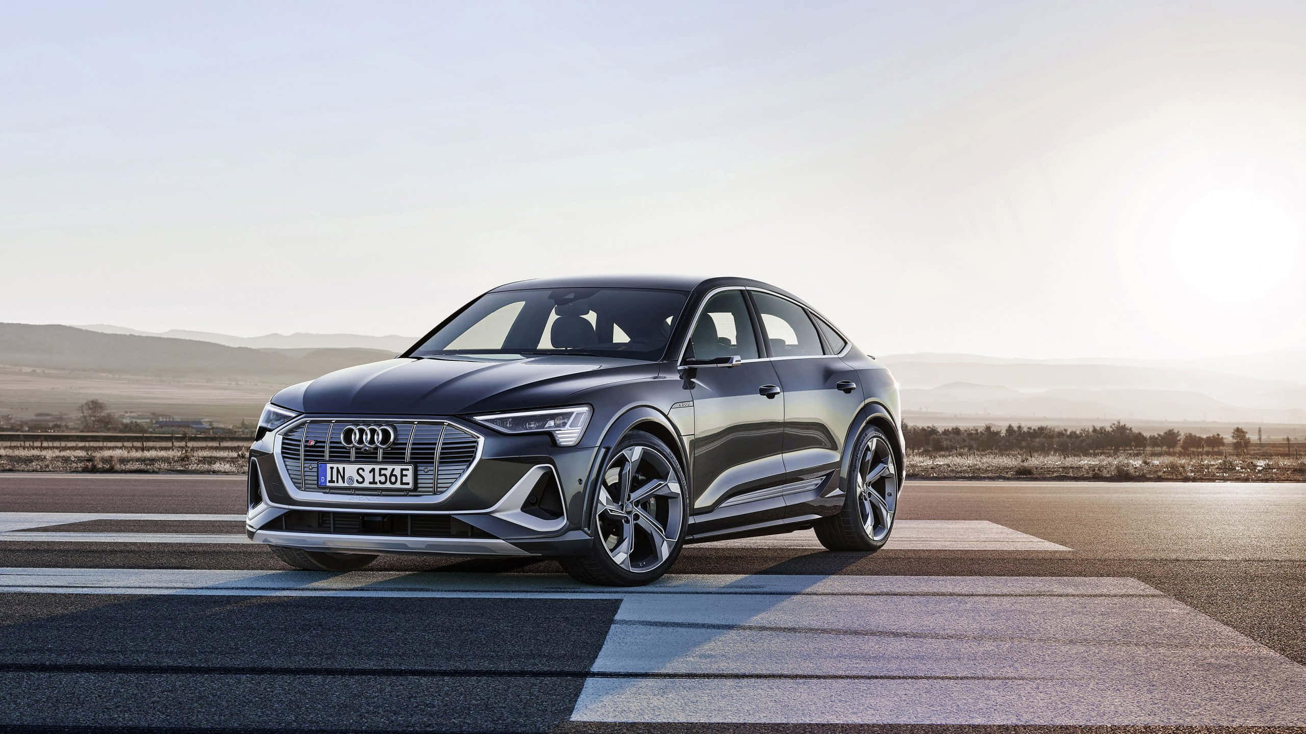 奧迪 桌布 壁紙 — 一台時尚的深灰色Audi e-tron S停在陽光普照的道路上，背景是連綿起伏的山丘。