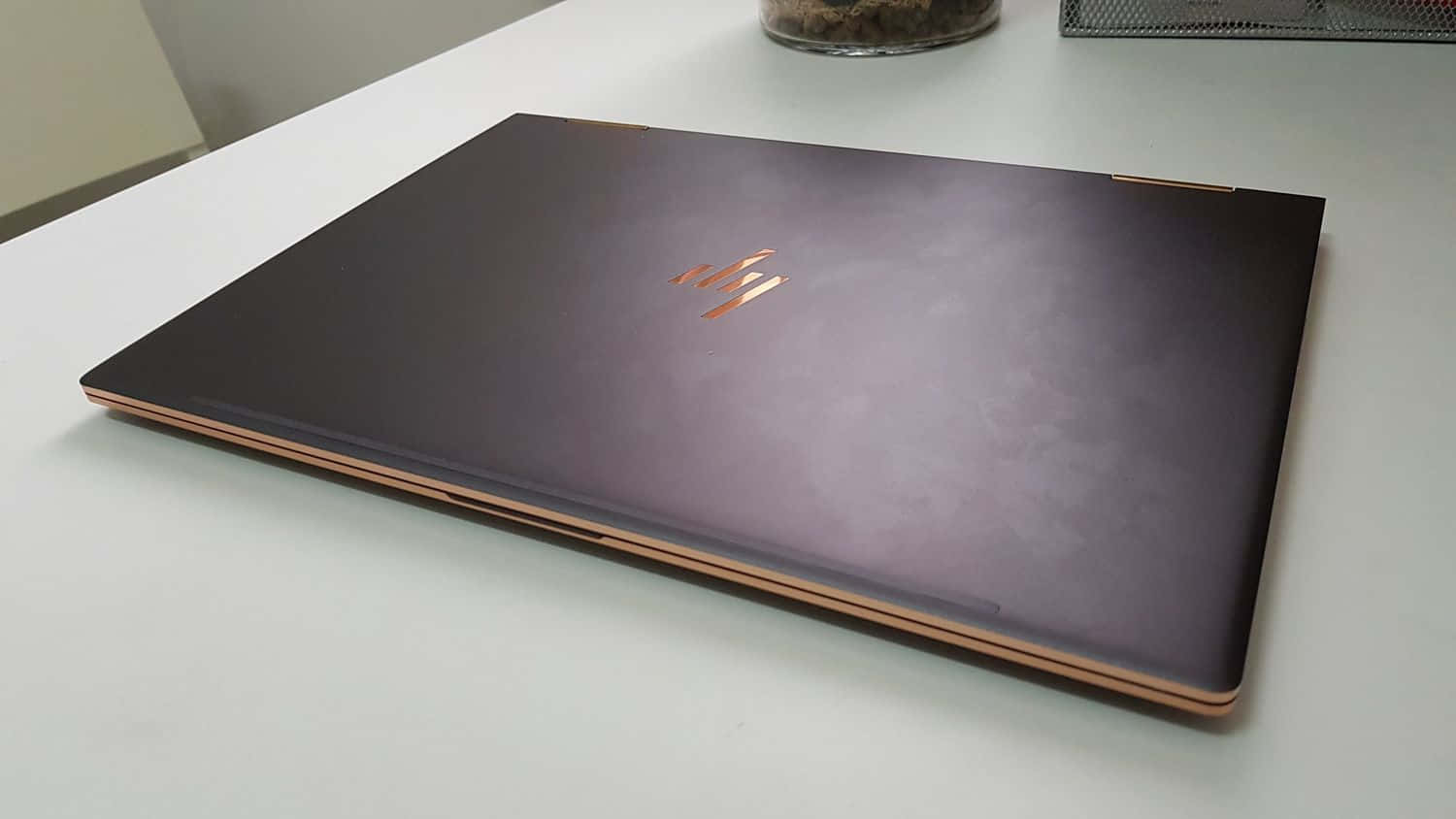 HP 桌布 壁紙 — 一台時尚的深紫色筆記型電腦，帶有玫瑰金色飾邊，闔上放在白色桌面上。