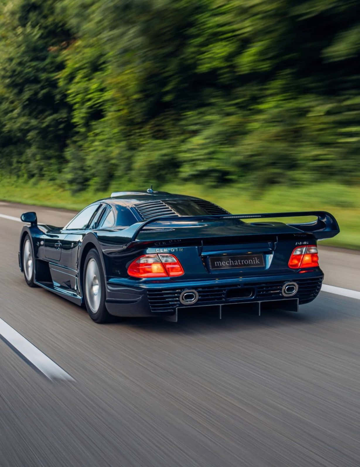 藍色 桌布 壁紙 — 一台時尚的深藍色 Mercedes CLK GTR 在樹林環繞的道路上疾馳，動態模糊效果突顯其力量與速度。