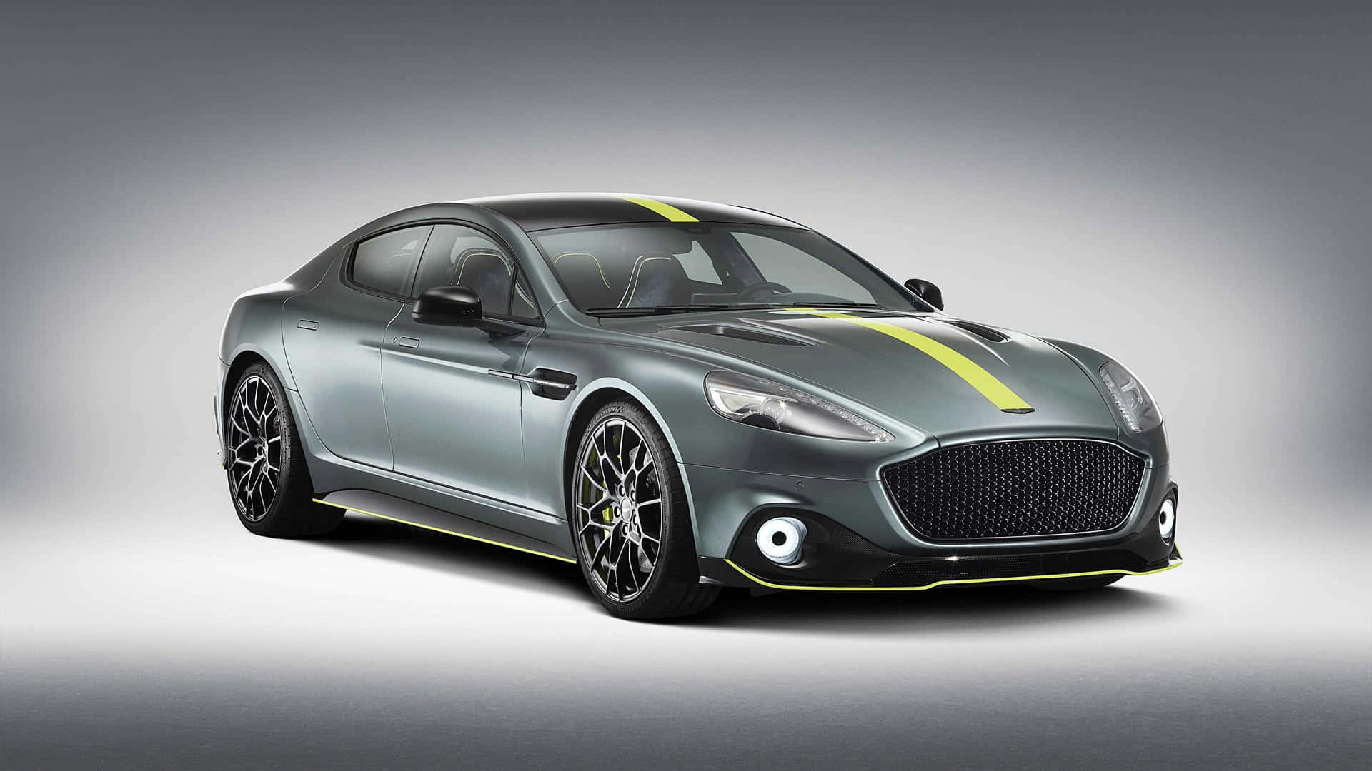 Aston Martin Rapide S 桌布 壁紙 — 一台時尚的灰色 Aston Martin，帶有醒目的黃色賽車條紋和黑色輪圈，在漸變灰色工作室背景前展示。